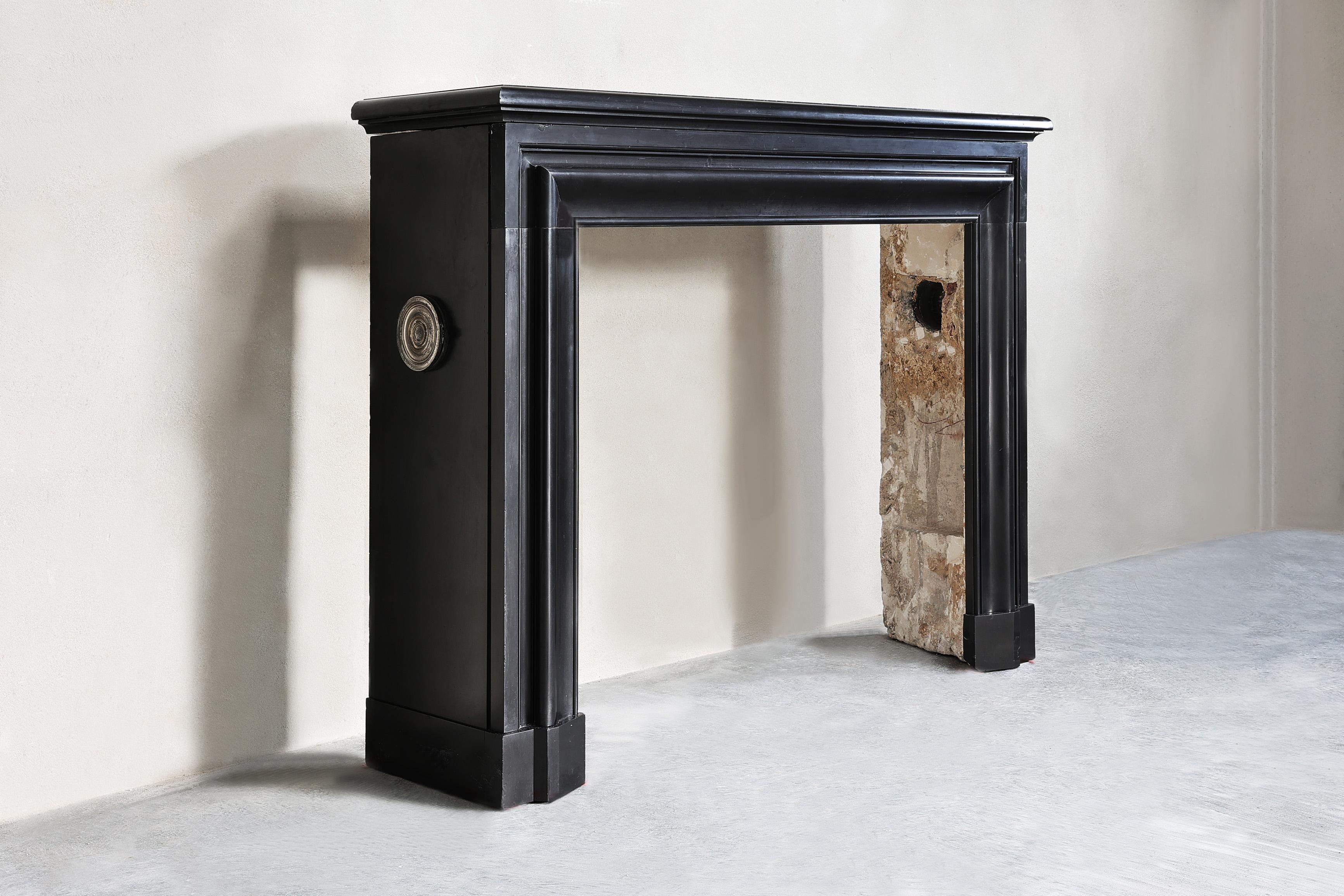 Beautiful antique mantelpiece made of Noir de Mazy marble in the style of Louis XVI. A fireplace from the 19th century with a sleek and chic look! The original grilles are still present on the sides of the mantelpiece.