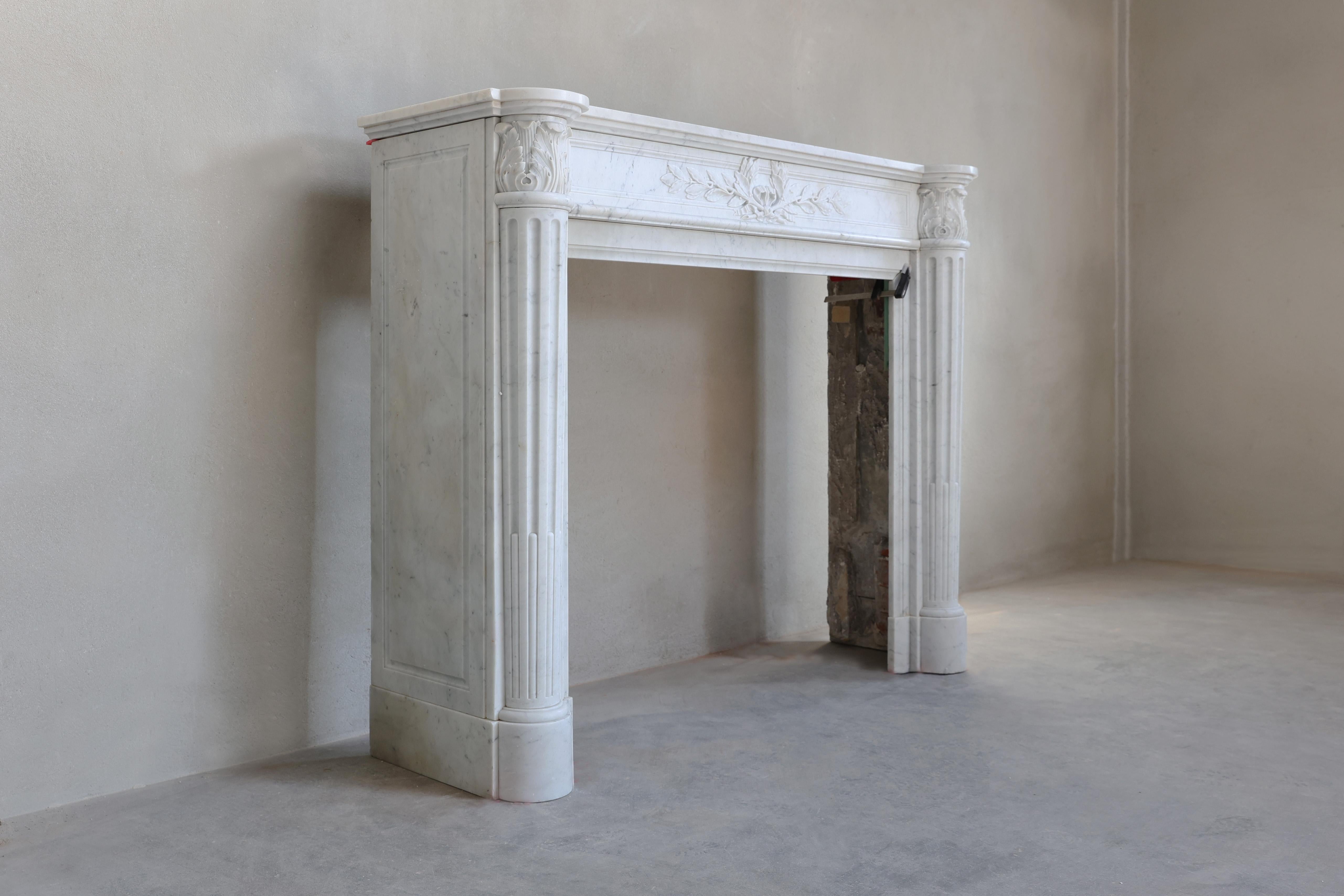 Beautiful antique fireplace carved in Carrara marble. This fireplace is in Louis XVI style and dates from the mid-19th century! The middle part is beautifully decorated with a laurel wreath and on the legs you can see the acanthus leaves. The legs