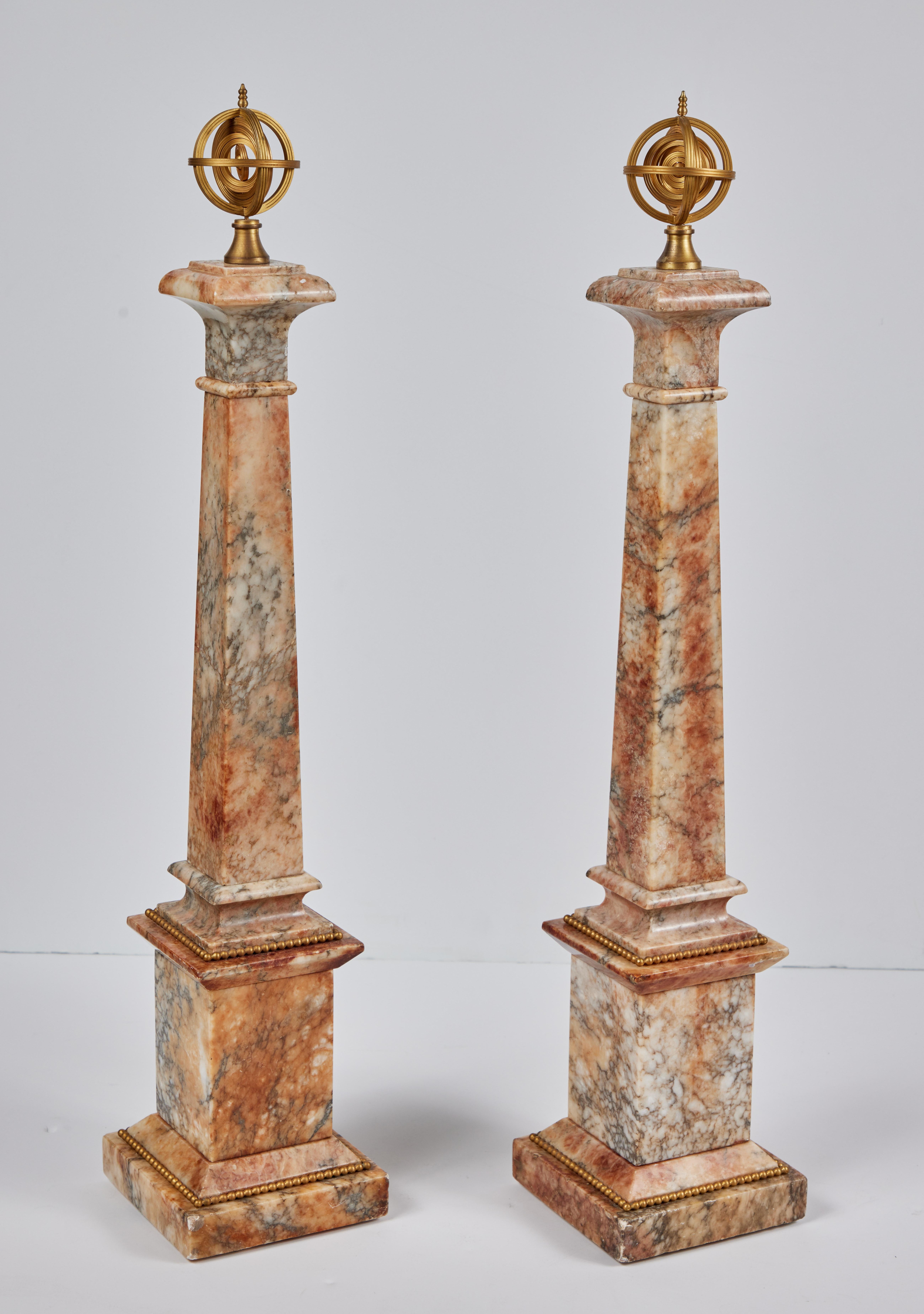 A pair of c. 1850, hand-carved, polished marble obelisks surmounted by gilt bronze armillary spheres. Each on raised bases embellished with strings of gilt bronze, pearl-form mounts.