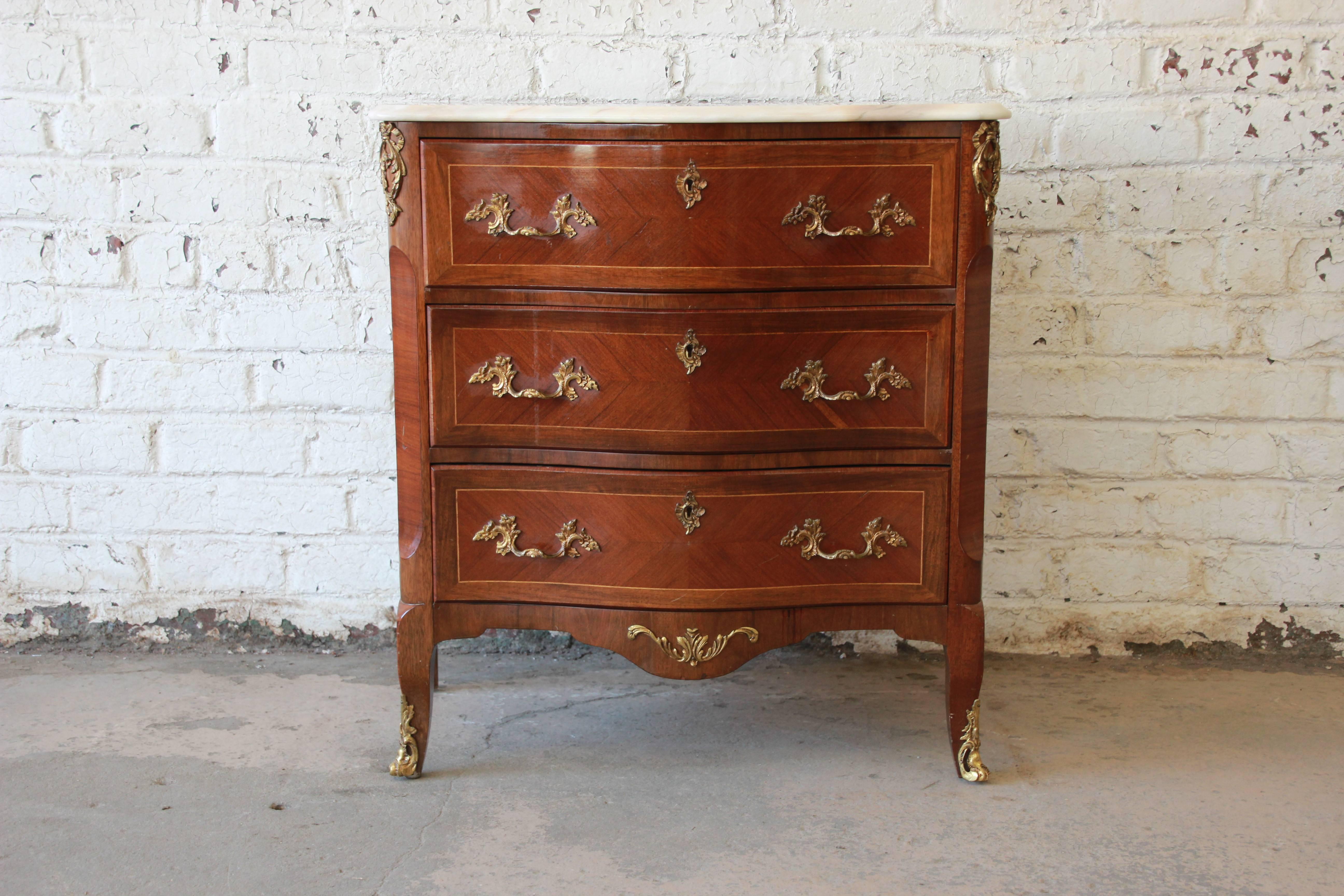Offering a beautiful XV style commode with a marble top and bronze ormolu. The chest offers three large drawers for storage options with nice accented bronze ormolu. It also features parquetry design on the drawers and sides of the cabinet. The