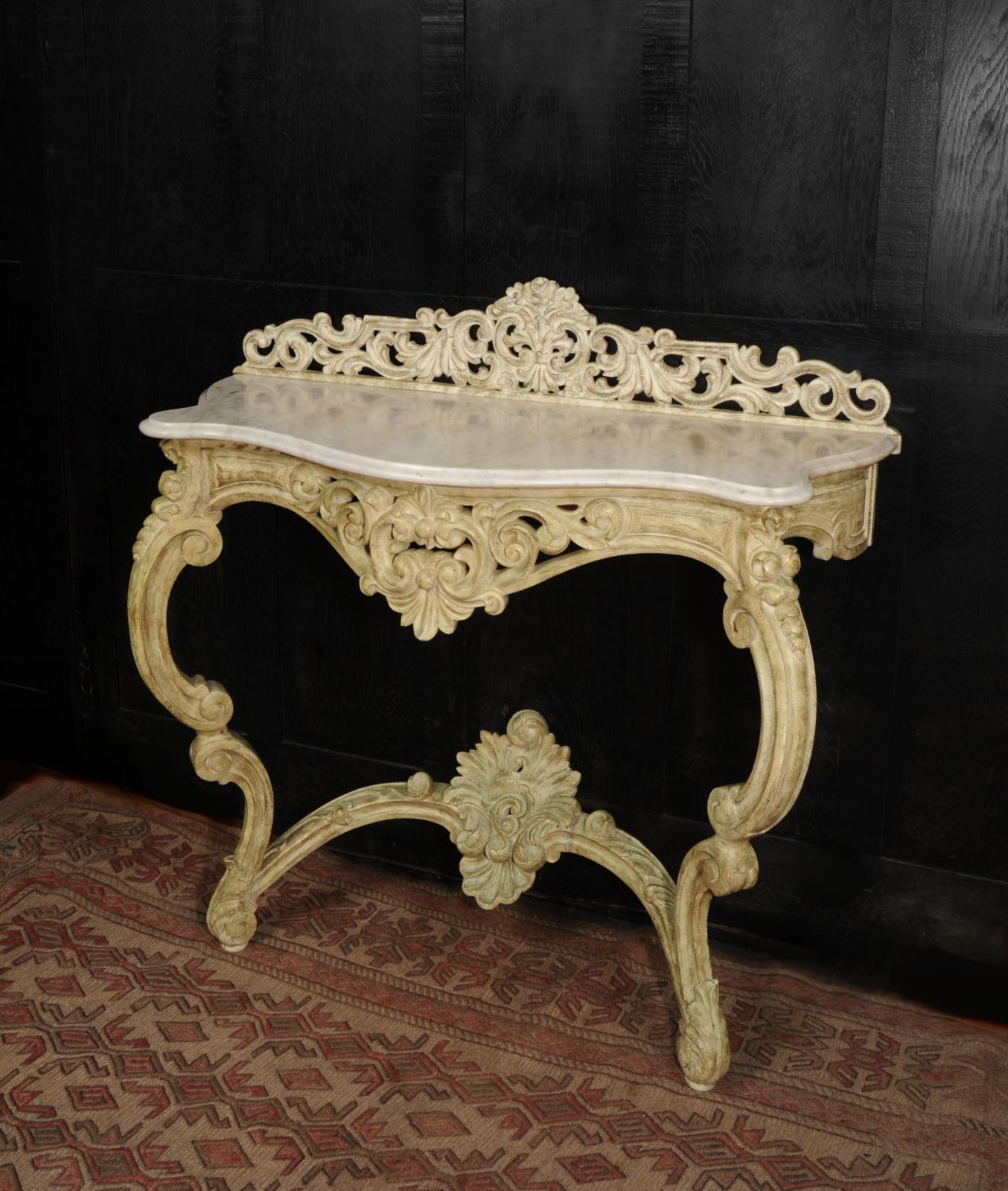 A beautiful carved and painted late Victorian Rococo console table with a Carrara marble top. It is beautifully carved in a hard wood, most likely mahogany, with bold scrolls and acanthus, and an arched stretcher with a flamboyant shell motif. It