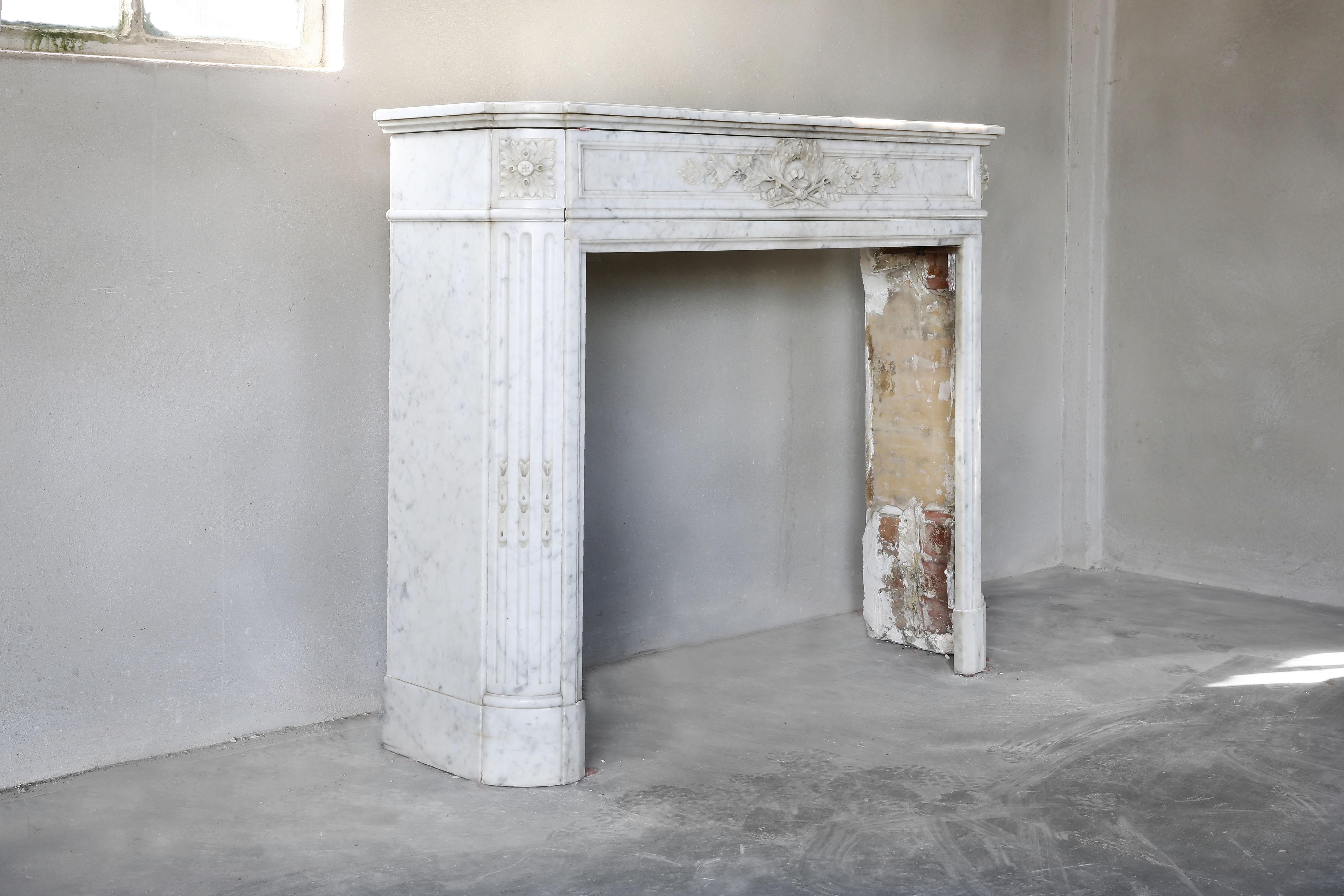 Beautiful compact antique marble fireplace from the marble Carrara from Italy. A mantelpiece from the 19th century in the style of Louis XVI. The mantelpiece has a Classic look and features a decorative ornament in the middle, flutes on the legs and