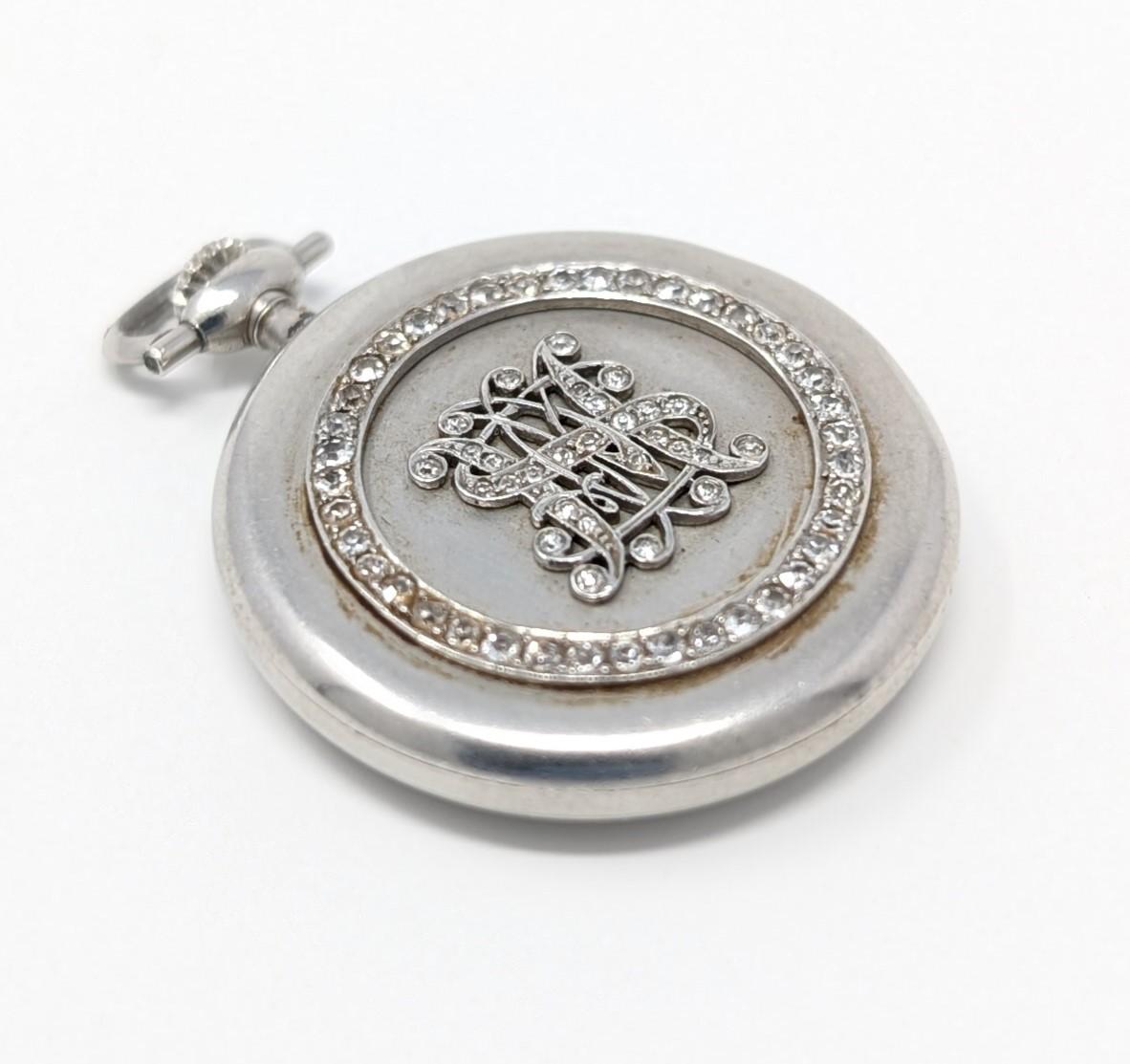 Antiguo reloj de bolsillo Marcus & Co. con deslumbrantes diamantes engastados en platino. Con un monograma en el centro, este pequeño pero precioso reloj mide 2,5 cm de diámetro con una caída total de 2,5 cm y 6 mm de profundidad.