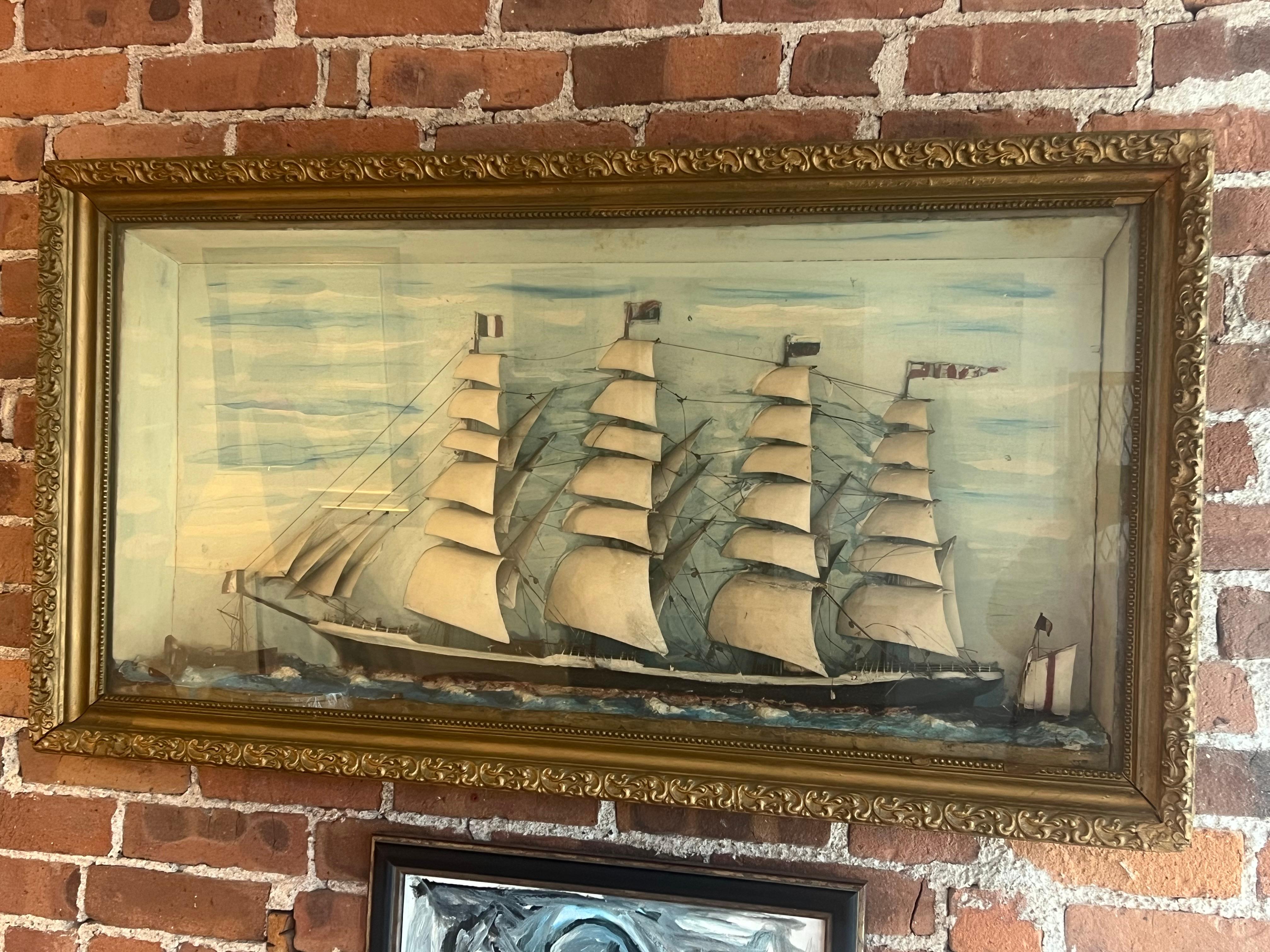 A commanding antique maritime shadow box diorama, featuring a four-masted clipper ship at full sail beneath a painted sky. Crafted with layered sails, hand-strung rigging, and three-dimensional relief details, this folk art tableau is housed in its
