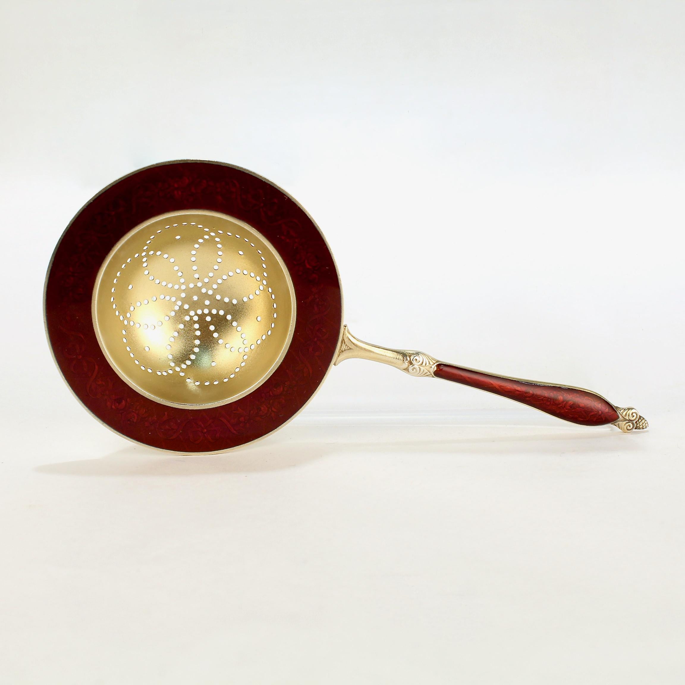 Ein sehr schönes norwegisches Teesieb von Marius Hammer.

Mit rotem Emaille-Dekor auf der Oberseite, einem Blumenmuster auf der Oberseite und einer goldfarbenen Oberfläche. 

Monogrammiert auf der Rückseite mit einem C.

Ein wunderschönes antikes