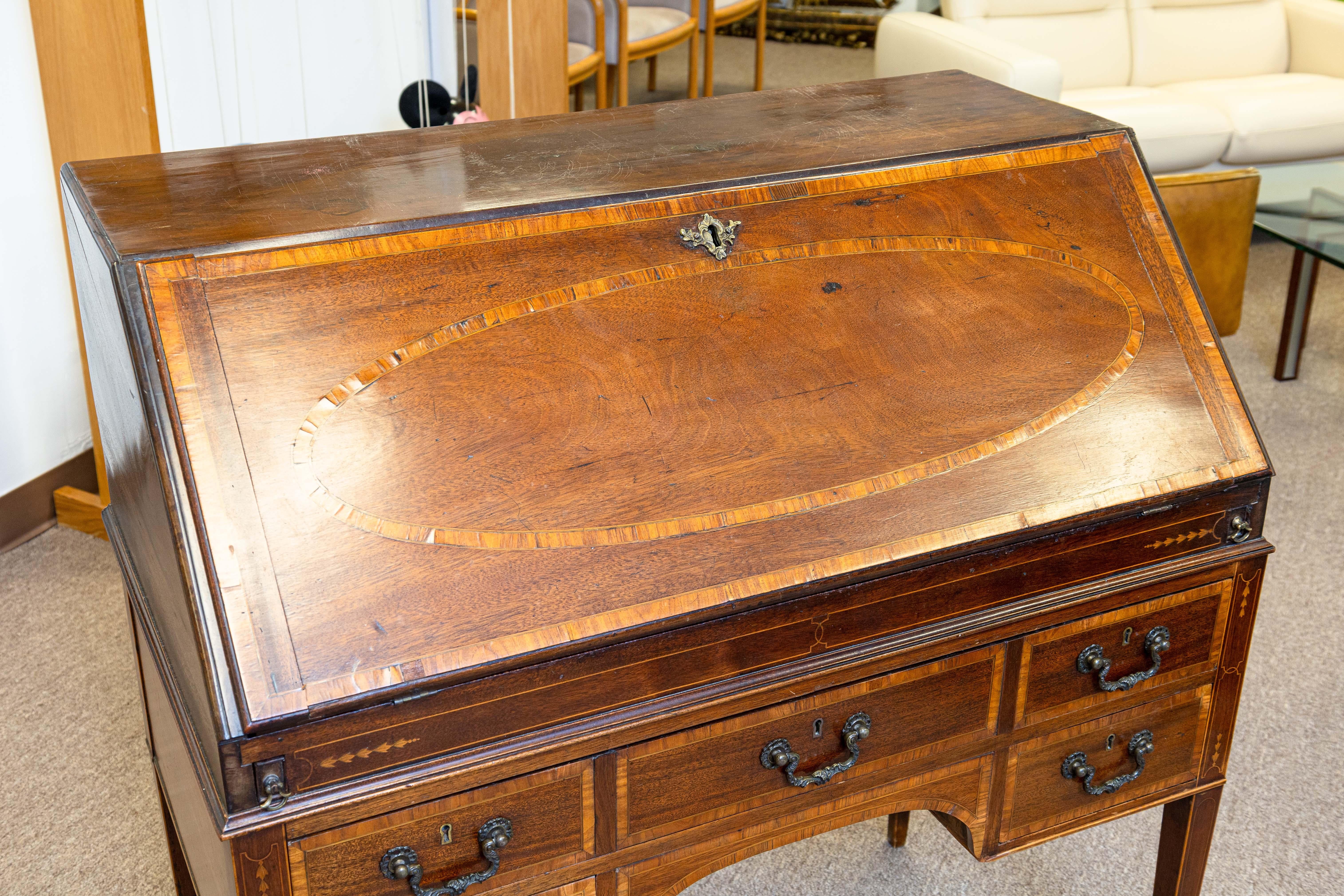 An antique marquetry writing secretary desk with inlaid patterns. Brass plaque on lever and etched “Made in England”. Circa early 20th century. Front drop leaf secretary with many drawers for storage and space for storage. The perfect fusion of