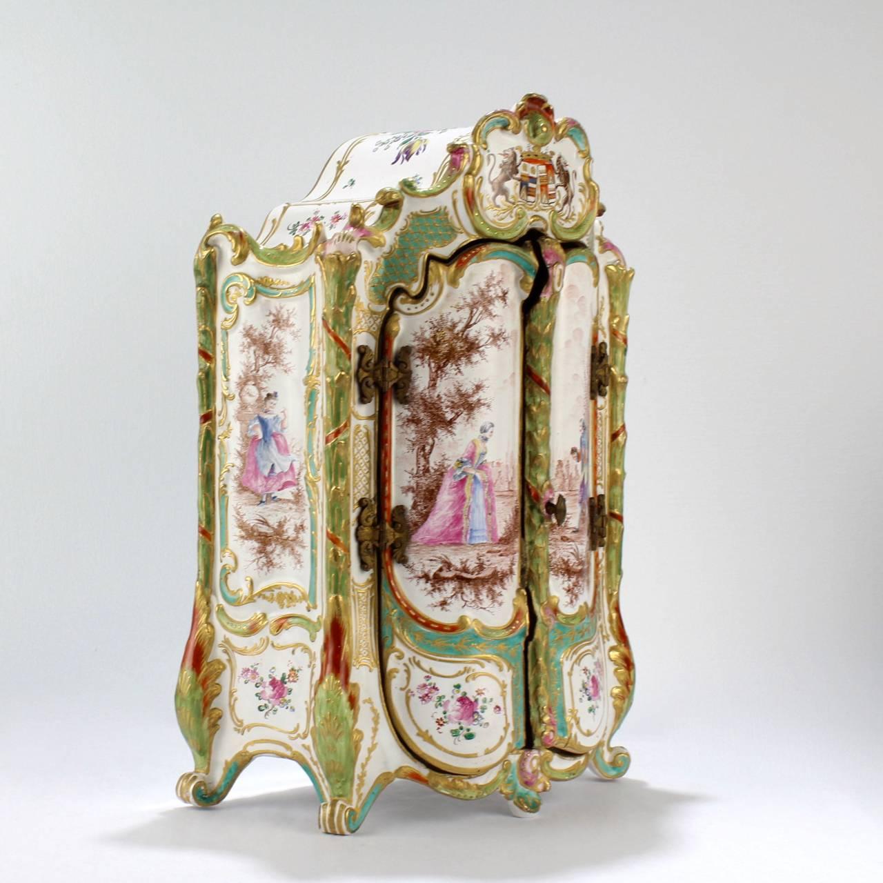 A wonderful antique miniature French faience armoire or jewelry casket.

The rococo form has finely hand painted scenes of lovers in formal garden settings and is richly decorated with floral bouquets, garlands, and swags, as well as with a faux