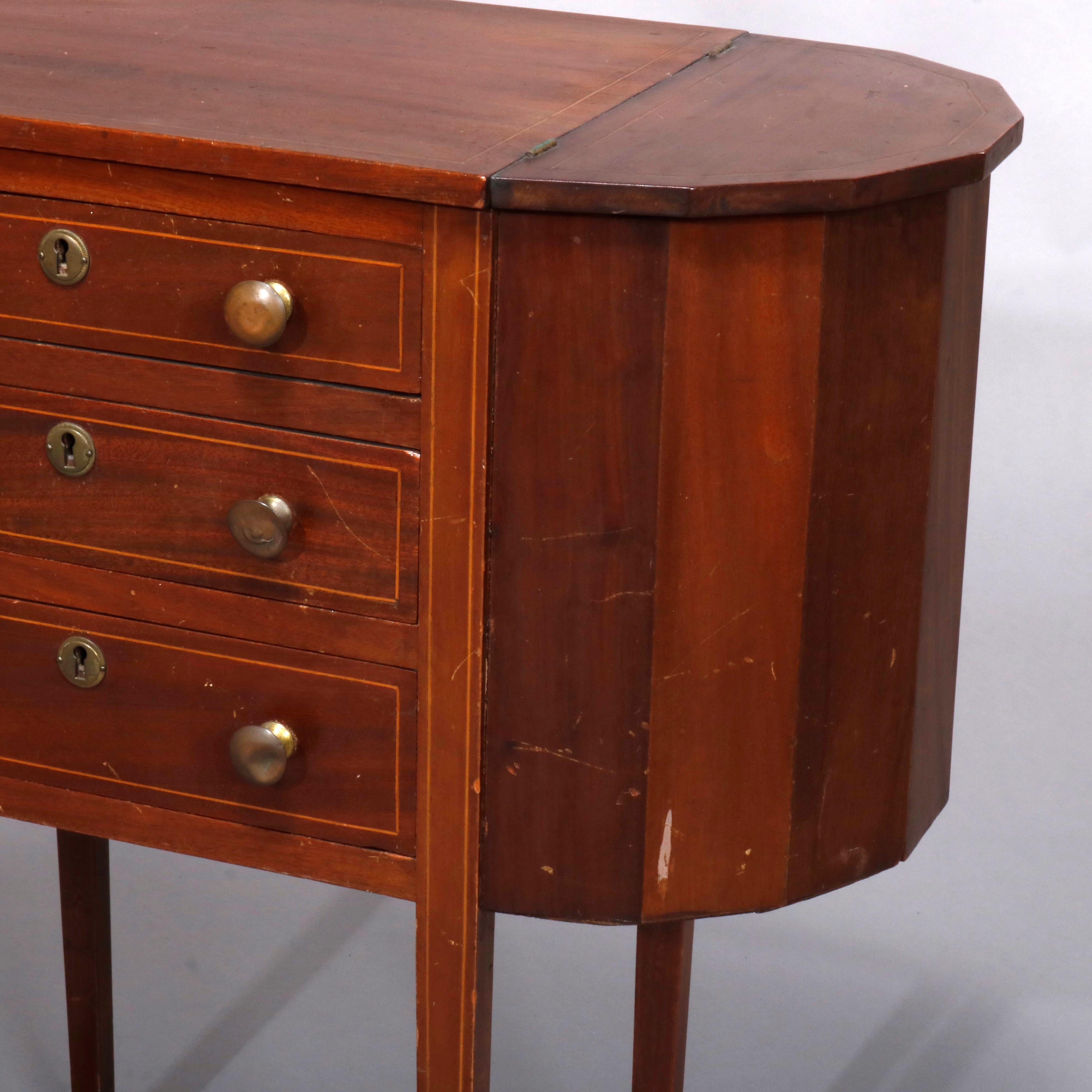 An antique Martha Washington sewing stand or cabinet offers mahogany construction with 
central tower having graduated drawers and flanked by faceted demilune project pockets, raised on tapered satinwood banded square legs, circa 1930

Measures-