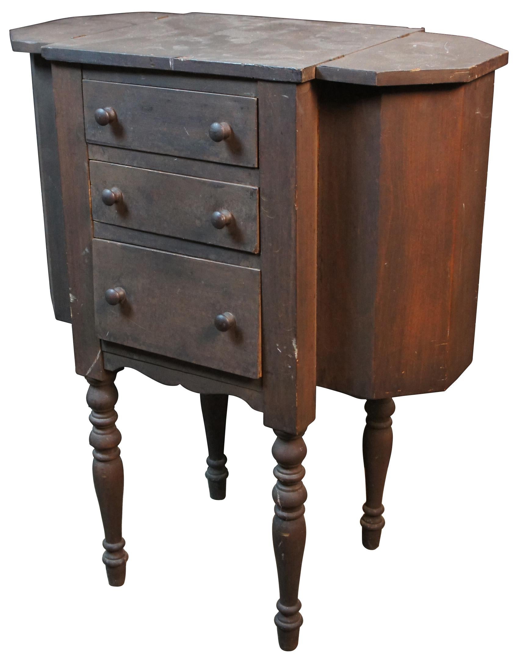 Antique Martha Washington style wooden sewing cabinet with two flip top end sections, three drawers, and turned spindle legs. Measure: 29