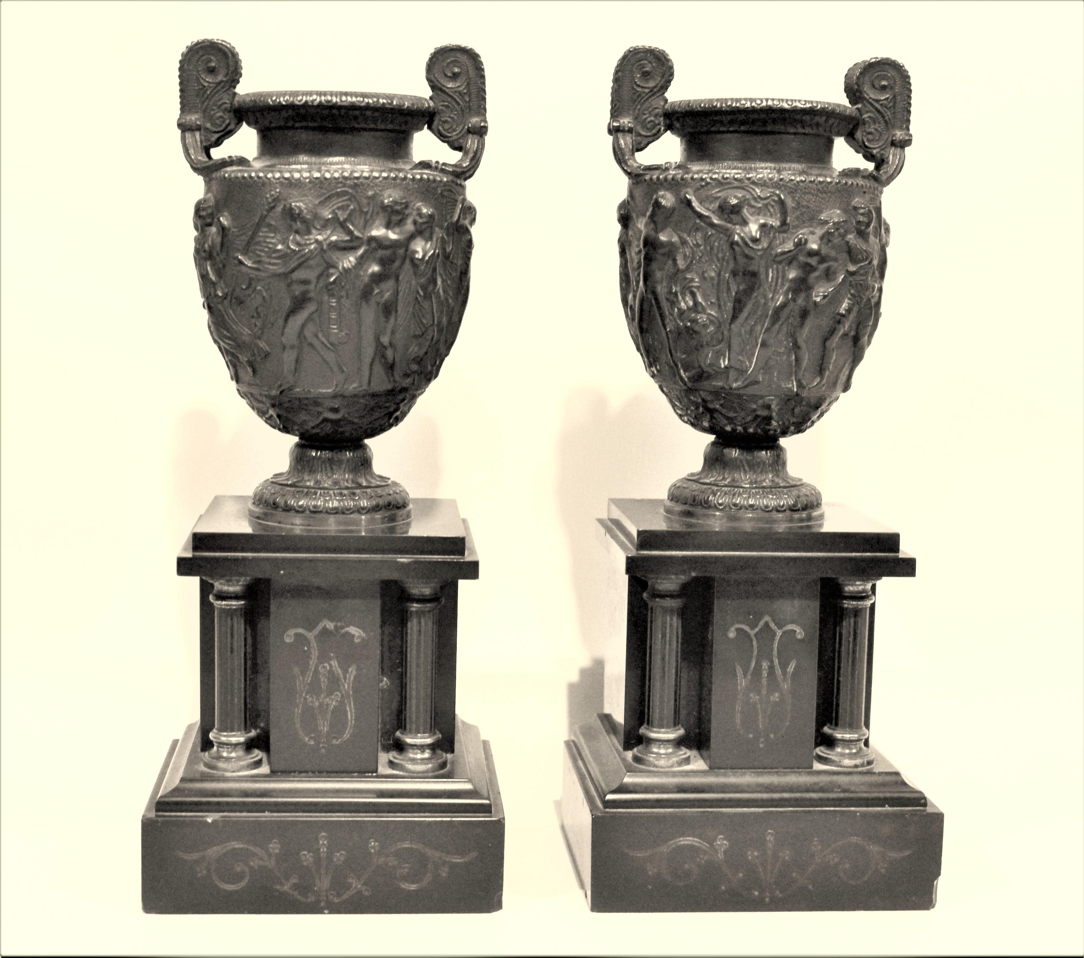 Pair of matching antique garnitures done with cast bronze urns with intricately cast neoclassical decoration in high relief presented on polished black slate pedestal bases with etched decoration.