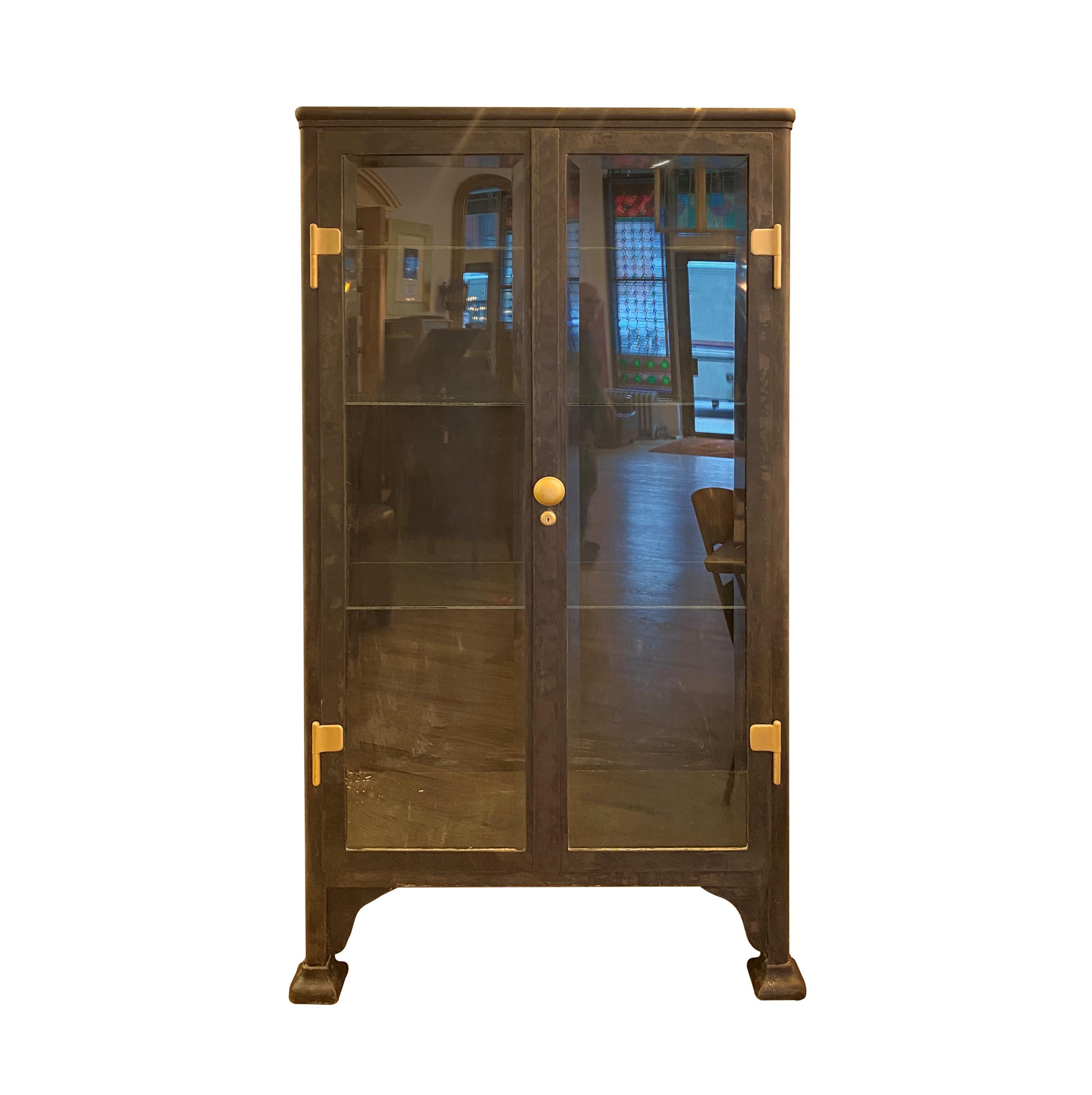 Antique 1020s cast iron double door medicine cabinet with casters. Features four glass shelves and beveled glass doors and side panels. Comes with the brushed brass door hardware. Please note, this item is located in one of our NYC locations.