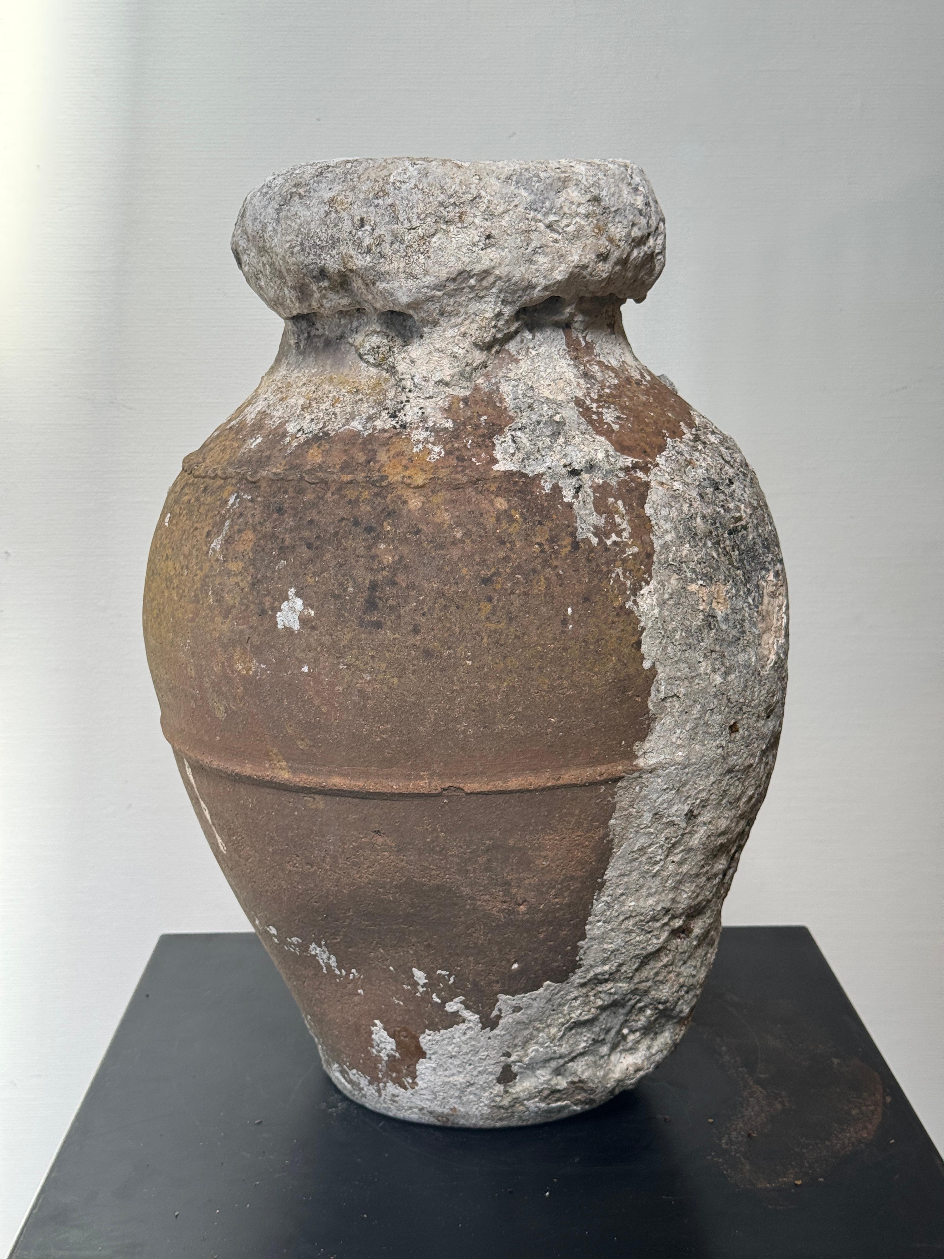 This monumental antique Mediterranean amphora-style vessel is a striking testament to ancient craftsmanship and the quiet poetry of time-worn material. Hand-formed from terracotta clay using traditional coil or wheel-throwing methods, the vessel