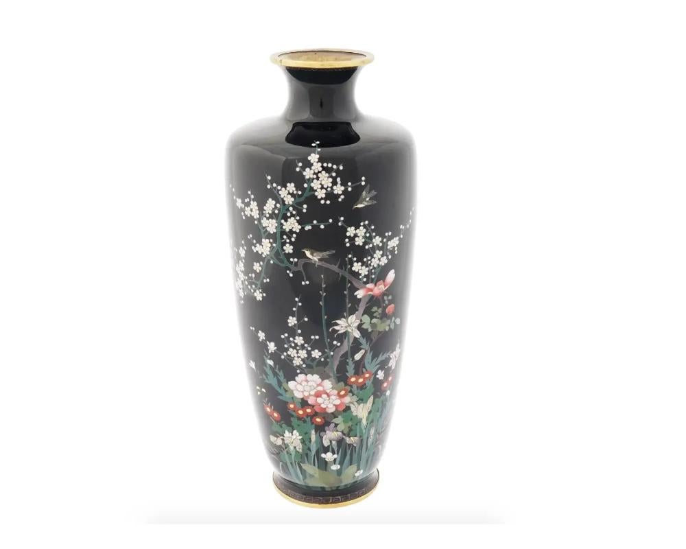 An antique Japanese Meiji Era brass and enamel vase, circa: early 20th century. The baluster form vase is enameled with polychrome images of blossoming flowers and plants and birds made in the Cloisonne technique on a black ground. The border of the