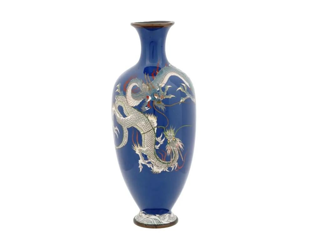 A large antique Japanese Meiji Era brass and enamel vase. Circa: early 20th century. The baluster form vase is enameled with a polychrome image of a pair of dragons made in the Cloisonne technique on a cobalt blue ground. The base is adorned with a
