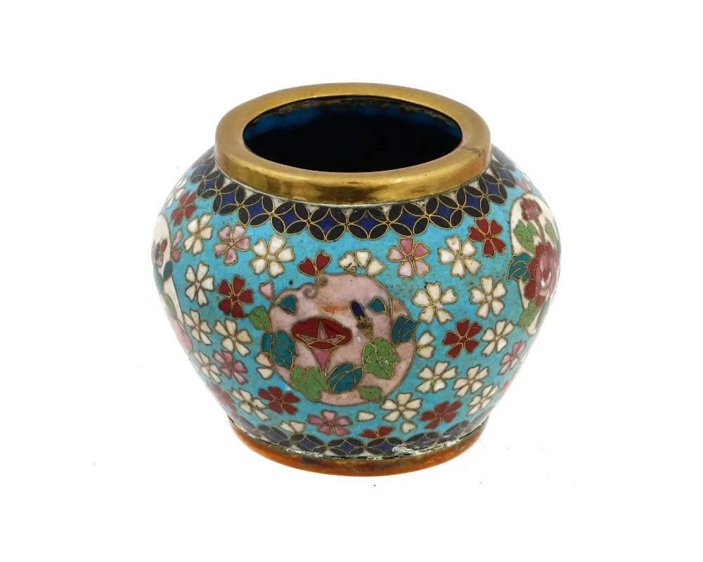 A miniature Japanese brass vase, early Meiji period, 1868 to 1912. of a globular form with a short and wide neck. The exterior is decorated with multiple polychrome enamel flowers and roundels with floral arrangements on a turquoise ground, the top