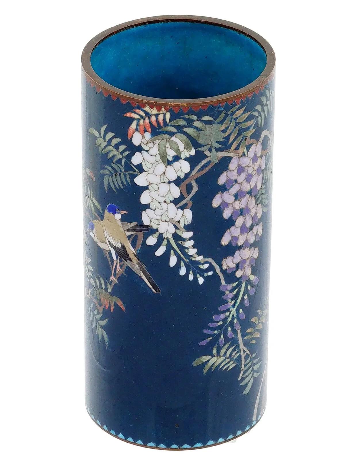 Un vaso a pennello giapponese in rame e smalto, attribuito a Goto


 Il vaso di forma cilindrica è ornato da un disegno policromo raffigurante uccelli con fiori di glicine in fiore realizzato con la tecnica Cloisonne su fondo blu. Il collo e la base