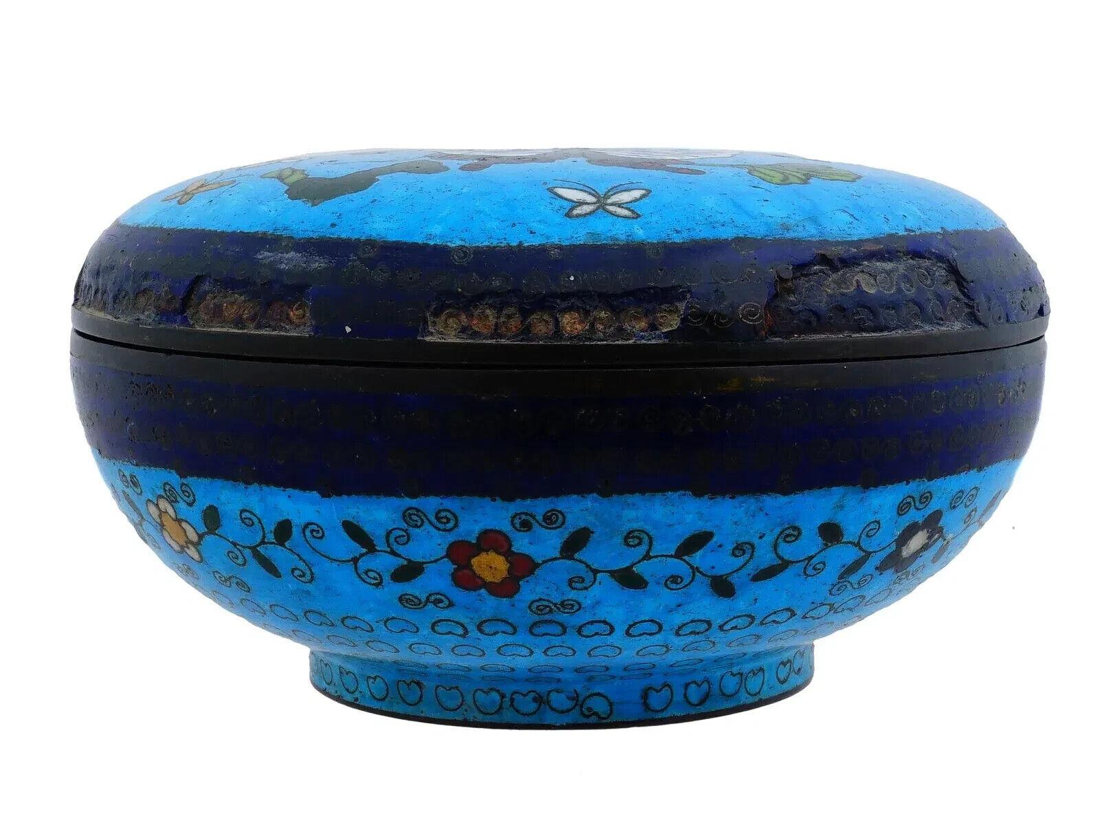 Un kogo o caja para incienso japonesa recubierta de esmalte sobre cobre. La tapa de la caja está esmaltada con un diseño policromado que representa mariposas en flores florecientes realizado en la técnica cloisonné. El cuerpo de la vajilla está
