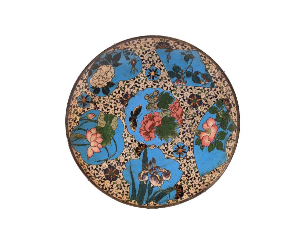 An antique Japanese, late Meiji era, enamel over gilt copper charger plate. The plate is adorned with polychrome enamel figural medallions made in the shape of a fan, a heart, a flower, and a diamond depicting blossoming flowers and butterflies on