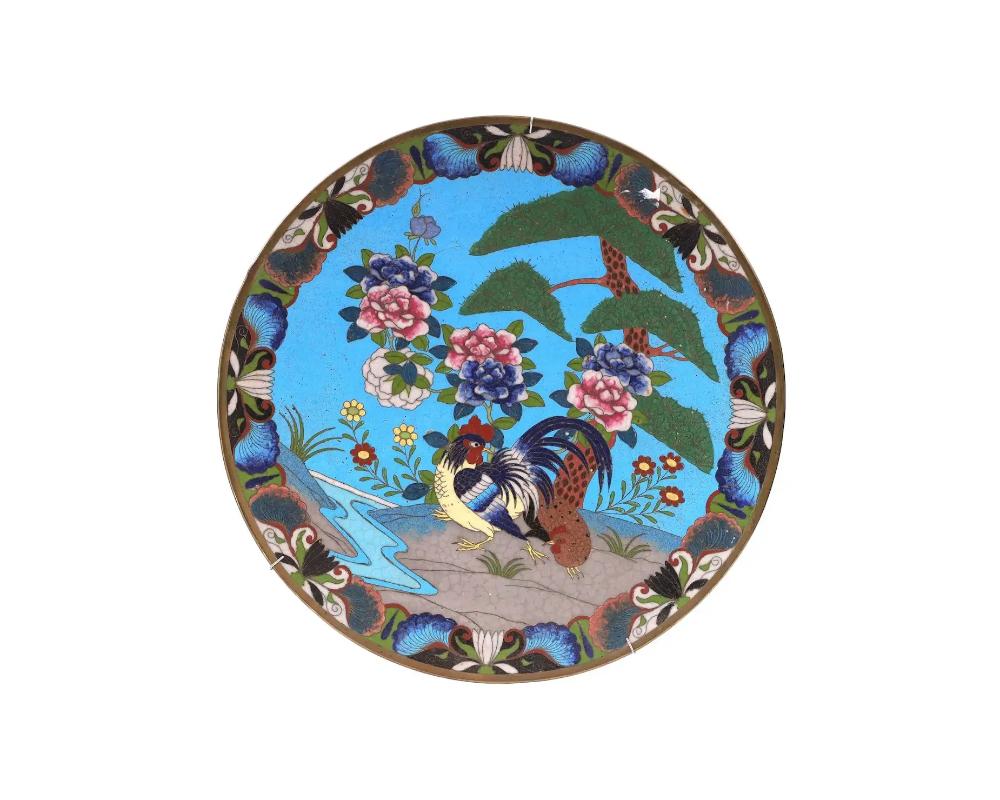 An antique Japanese, late Meiji era, enamel over copper charger plate. The plate is adorned with a polychrome scene with a rooster and a chicken on a pond with blossoming flowers and trees on the turquoise ground made in the Cloisonne technique. The