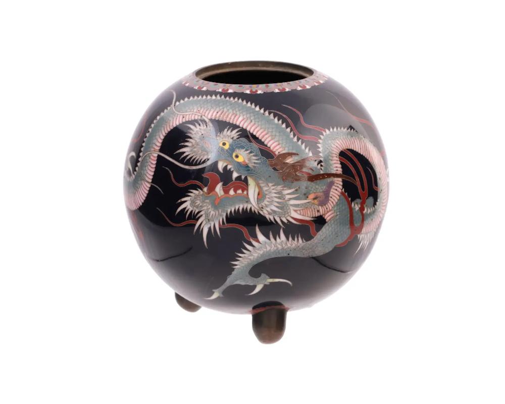 An antique Japanese, late Meiji Era, tripod enamel censer koro. The sphere form ware is enameled with a polychrome image of a dragon on a black ground made in the Cloisonne technique. The mouth of the ware is adorned with a foliage motif made in the