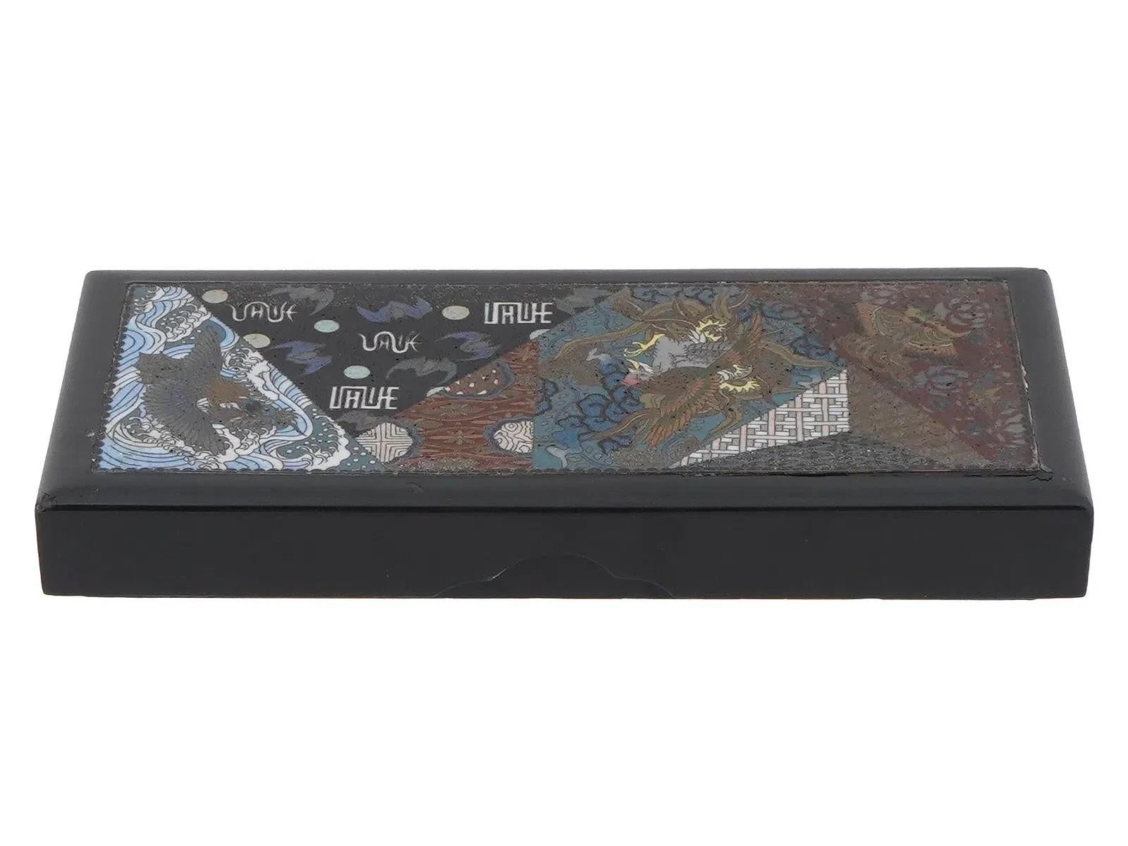 An antique Japanese enameled wooden box. Late Meiji period, before 1912. The box has a rectangular shape with a black border. The lid features a cloisonne enamel design with traditional Japanese motifs, including butterflies, phoenix, birds, waves,
