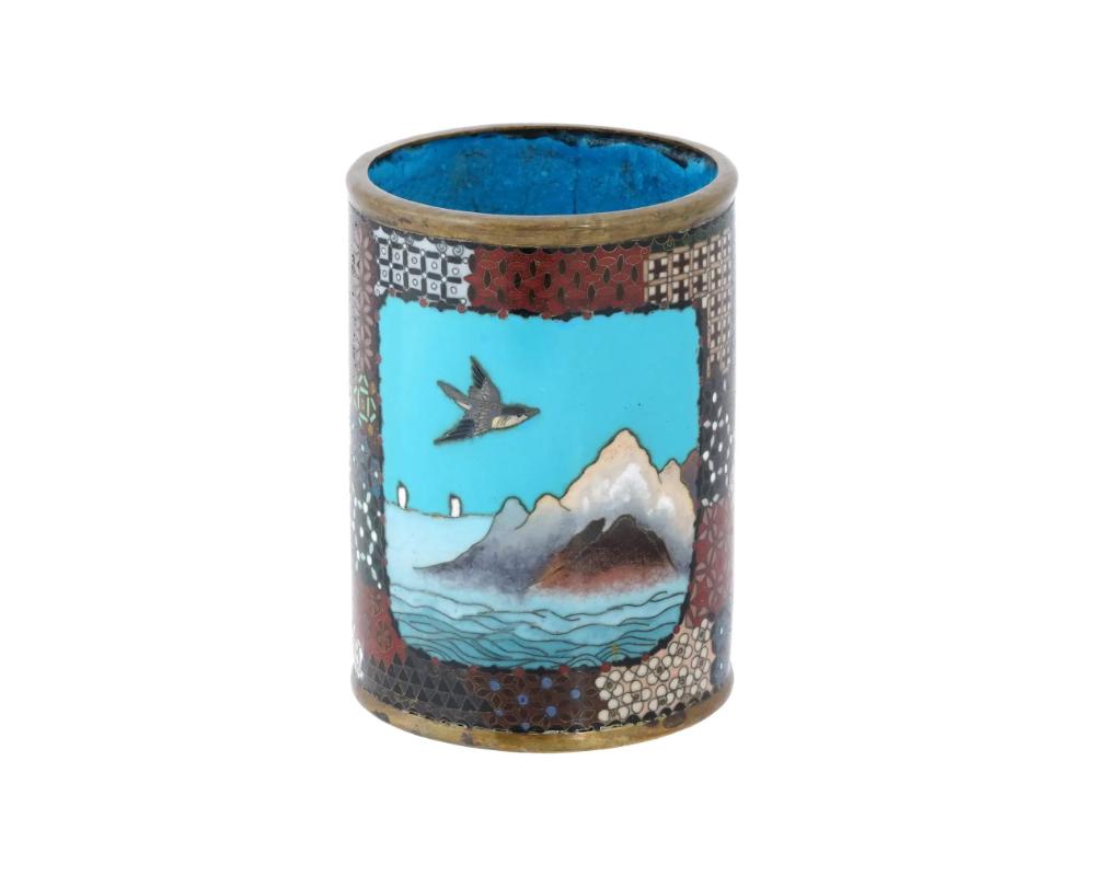An antique Japanese late Meiji Era cylindrical shaped enamel brush pot. Circa: late 19th century. The cylindrical form pot is enameled with polychrome medallions depicting a scene with a bird flying over a mountain river landscape, and butterflies