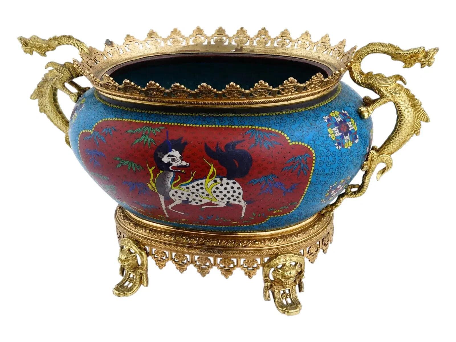 Antico vaso decorativo giapponese in smalto cloisonne con base e manici in bronzo dorato. Ha una forma arrotondata, simile a una ciotola, di colore blu con motivi floreali e vortici, ornata da due medaglioni rossi che raffigurano animali mitici: