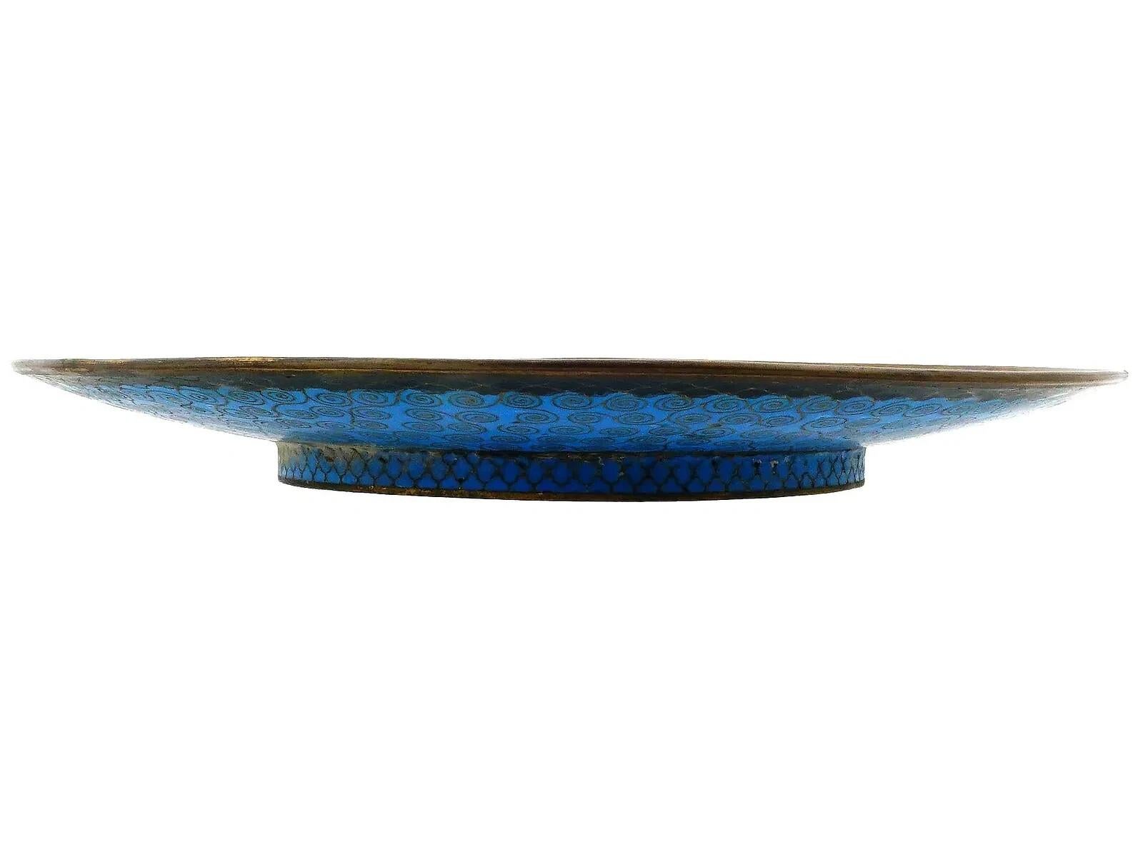 Un antico piatto giapponese in smalto cloisonne dell'epoca Meiji. Lo sfondo è di colore marrone scuro e presenta una gru bianca circondata da foglie di bambù verdi e piccoli fiori rosa. Il bordo del vassoio è decorato con un complesso motivo