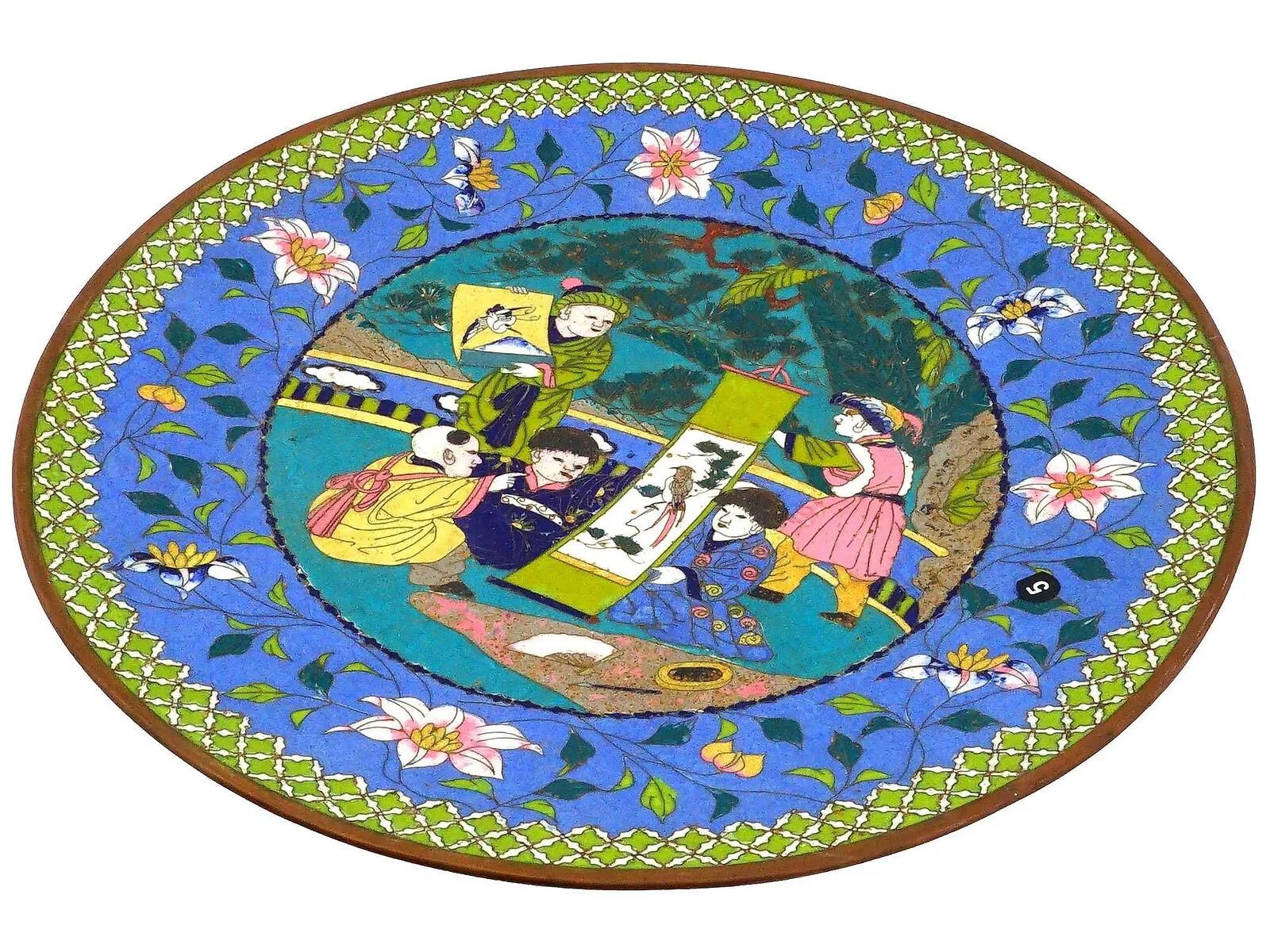 Assiette japonaise ancienne ornée d'un motif en émail cloisonné polychrome. La scène centrale met en scène plusieurs enfants. Le fond est un mélange vibrant de bleu et de turquoise, et la scène est décorée de motifs floraux sur la bordure, avec un