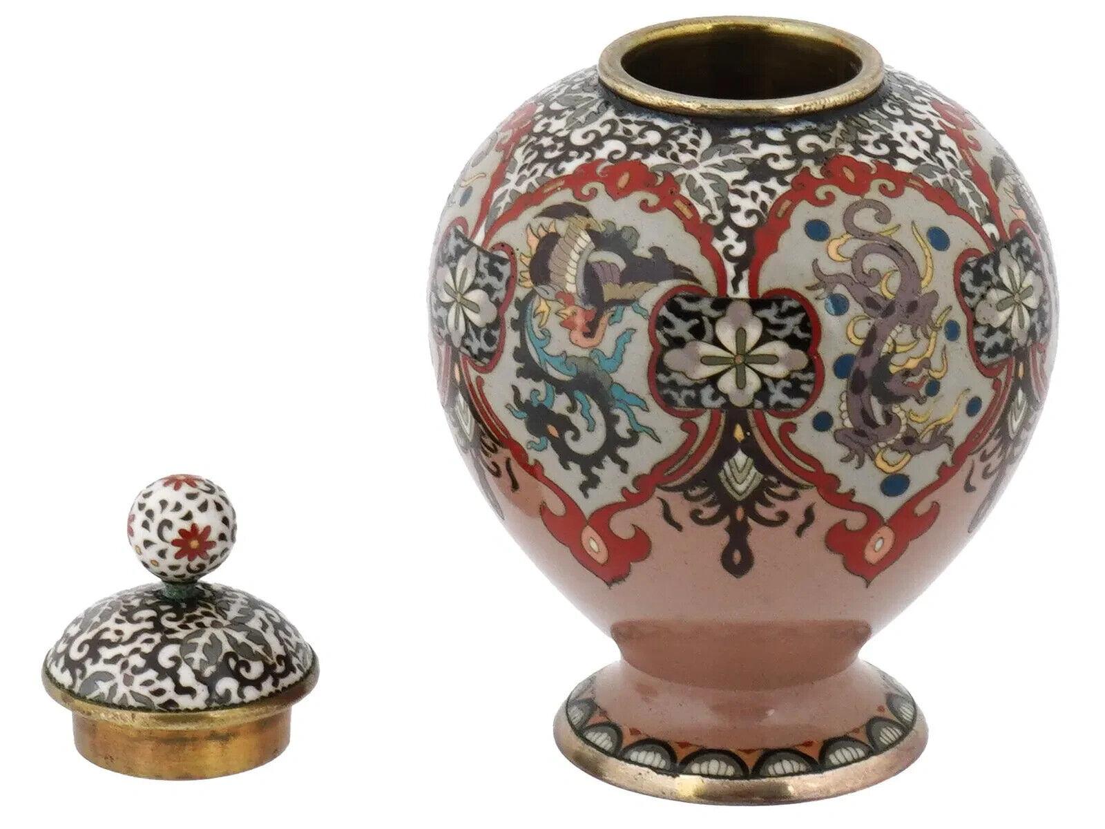 A fine quality antique Japanese cloisonne enamel lidded jar from the Meiji period, standing on a foot and featuring a lush decor with mythical animals and floral motifs on a pink background. The lid is adorned with a ball shaped handle. Collectible