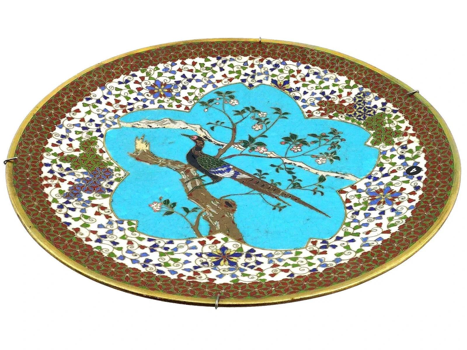 Un antico piatto smaltato giapponese dell'epoca Meiji. Il piatto è smaltato con l'immagine policroma di un uccello seduto su un ramo con fiori in fiore su un fondo blu turchese realizzato con la tecnica della cloisonne. Il bordo è decorato con un