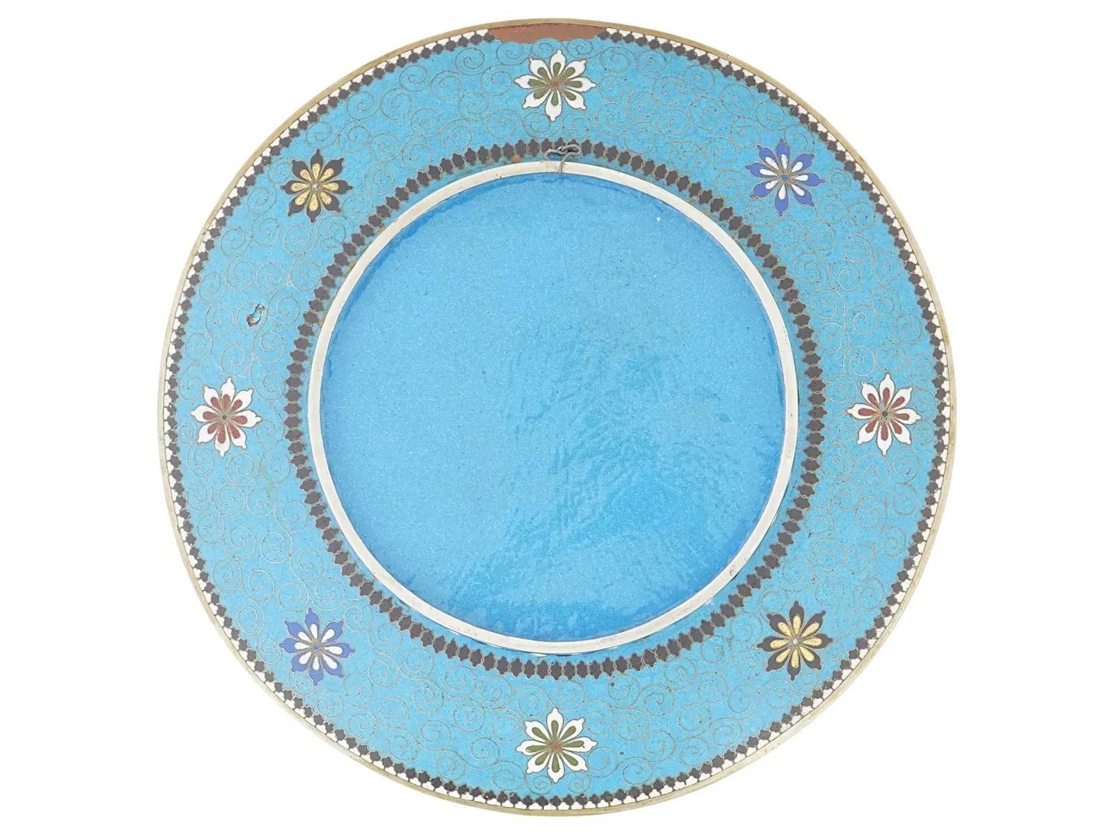 Antico piatto giapponese in smalto cloisonne del periodo Meiji con un suggestivo pannello centrale azzurro decorato con gru, piccoli uccelli, canne e piante fiorite. La scena è finemente dettagliata, con un'elegante lavorazione in oro e smalto