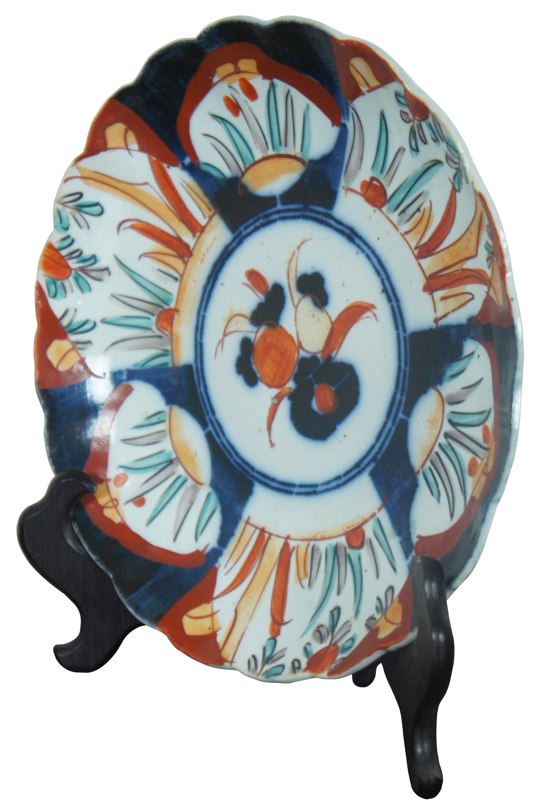 Antique Meiji period Japanese imari porcelain plate with scalloped edges and an orange and blue design of plants and flowers. Display on a folding wood stand.
 