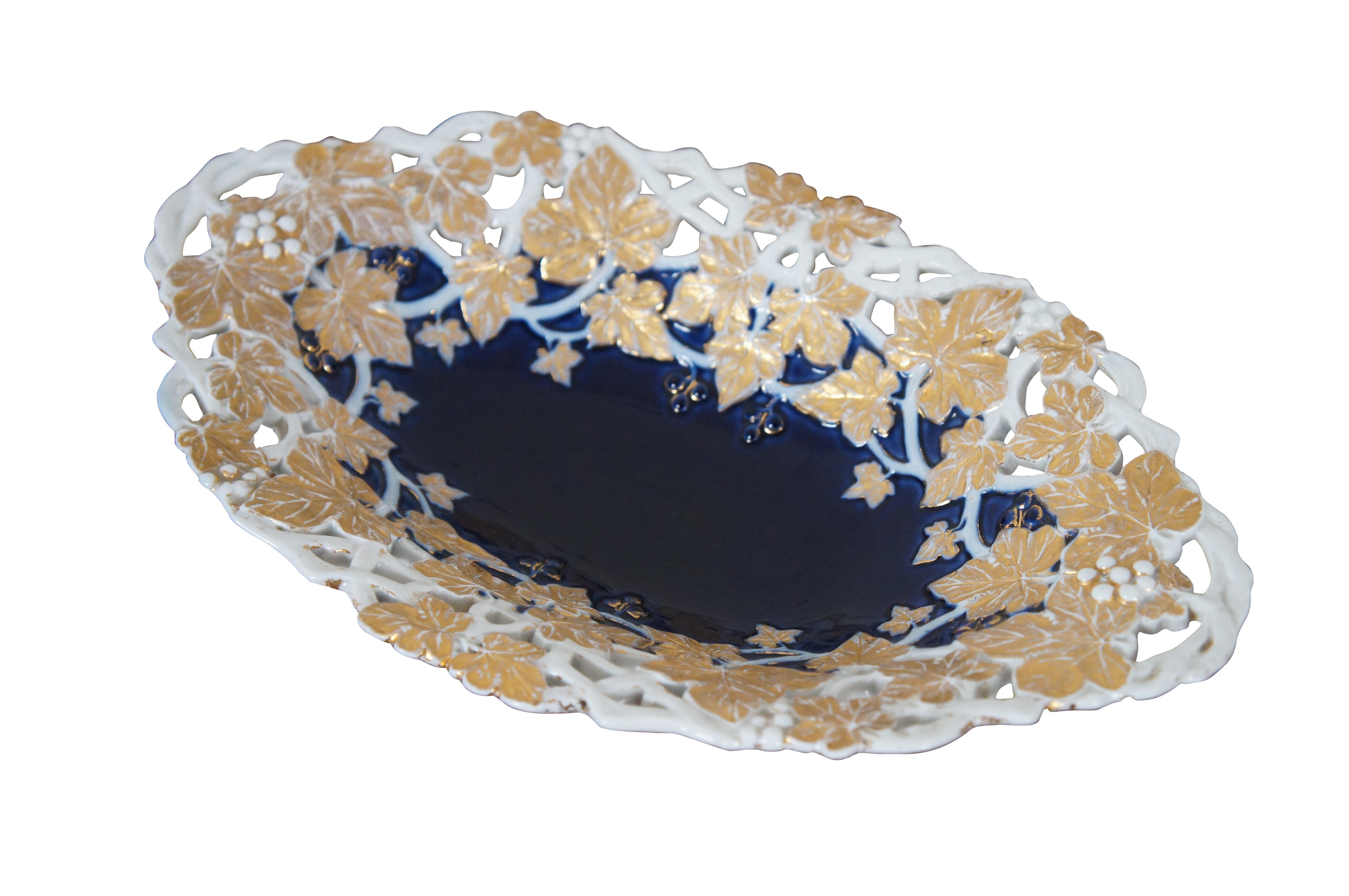 Antique German Dresden Meissen porcelain footed cabinet plate / centerpiece bowl / serving platter / compote featuring scalloped oval form with low relief reticulated design of gold gilt grapevines, grapes and leaves with cobalt blue center and