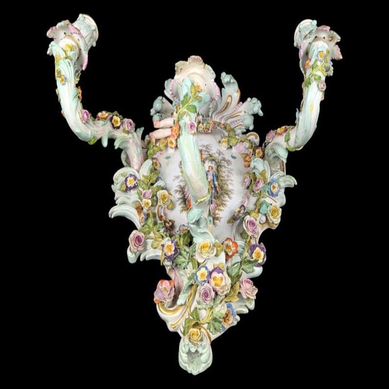 This exquisite antique Meissen three-arm candelabra wall light exemplifies the elegance and artistry of 18th-century German porcelain. Each arm is intricately designed and adorned with finely crafted floral details in vibrant shades of pink, blue,