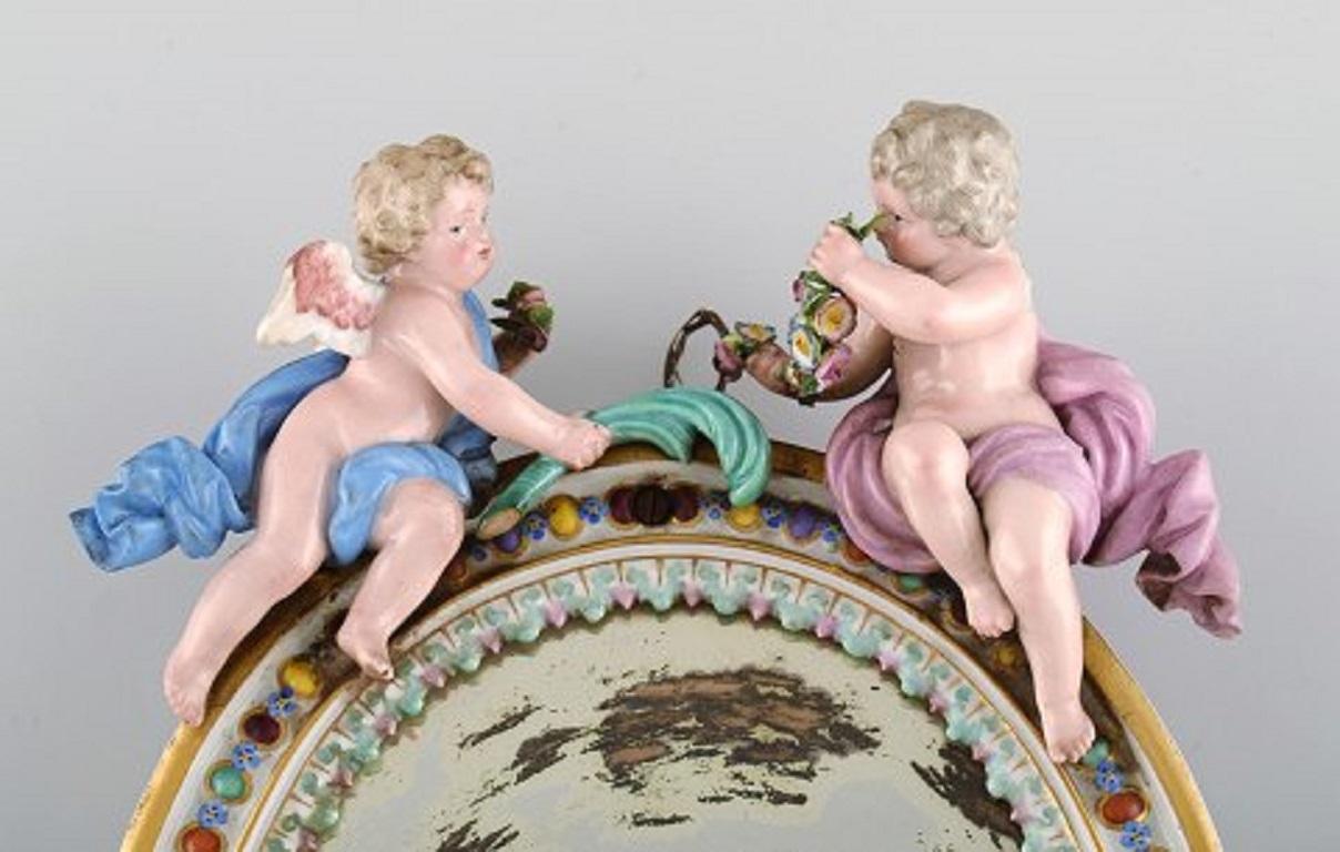 Antique Meissen porcelain mirror with original glass. Decorated with putti and moulded flowers.,
19th century.
Measures: 24.5 x 17.5 cm.
One wing is missing, another wing cut, small chips on moulded flowers.