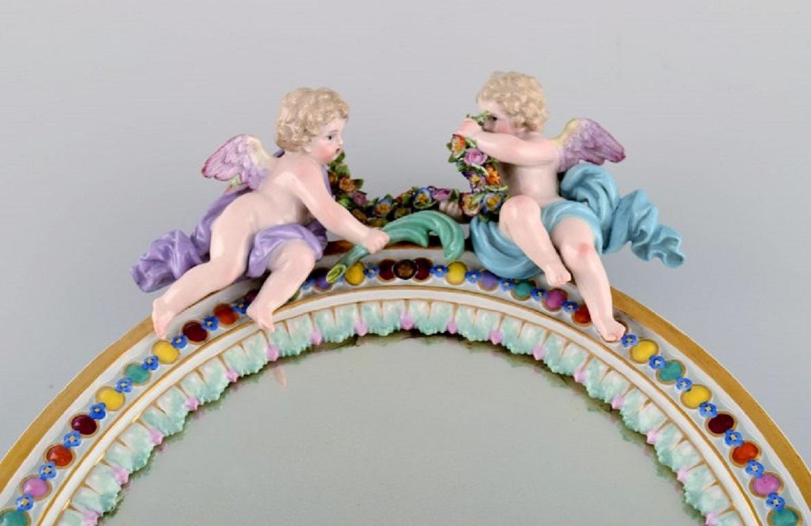 Antique Meissen porcelain mirror with original glass. Decorated with putti and moulded flowers. 
Approx. 1900.
Measures: 34.5 x 25.5 cm.
In excellent condition. One wing cut/ broken.
Stamped.
1st factory quality.