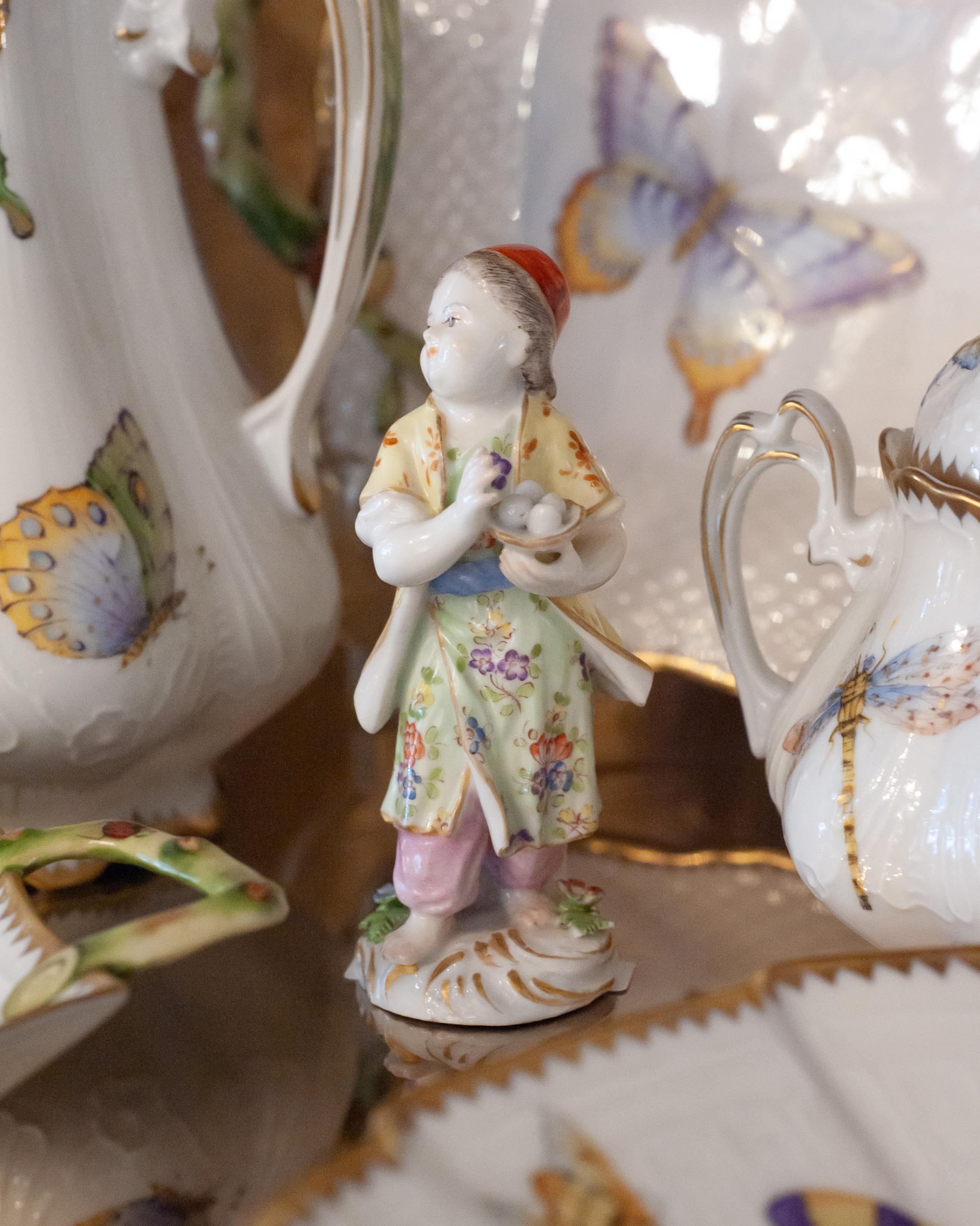 Un'ode all'eleganza della cineseria - Questa antica statuetta in stile Meissen incarna la grazia e l'estrosità del fascino europeo del XVIII secolo per l'Oriente. Finemente modellato e delicatamente dipinto a mano, cattura i dettagli raffinati e lo