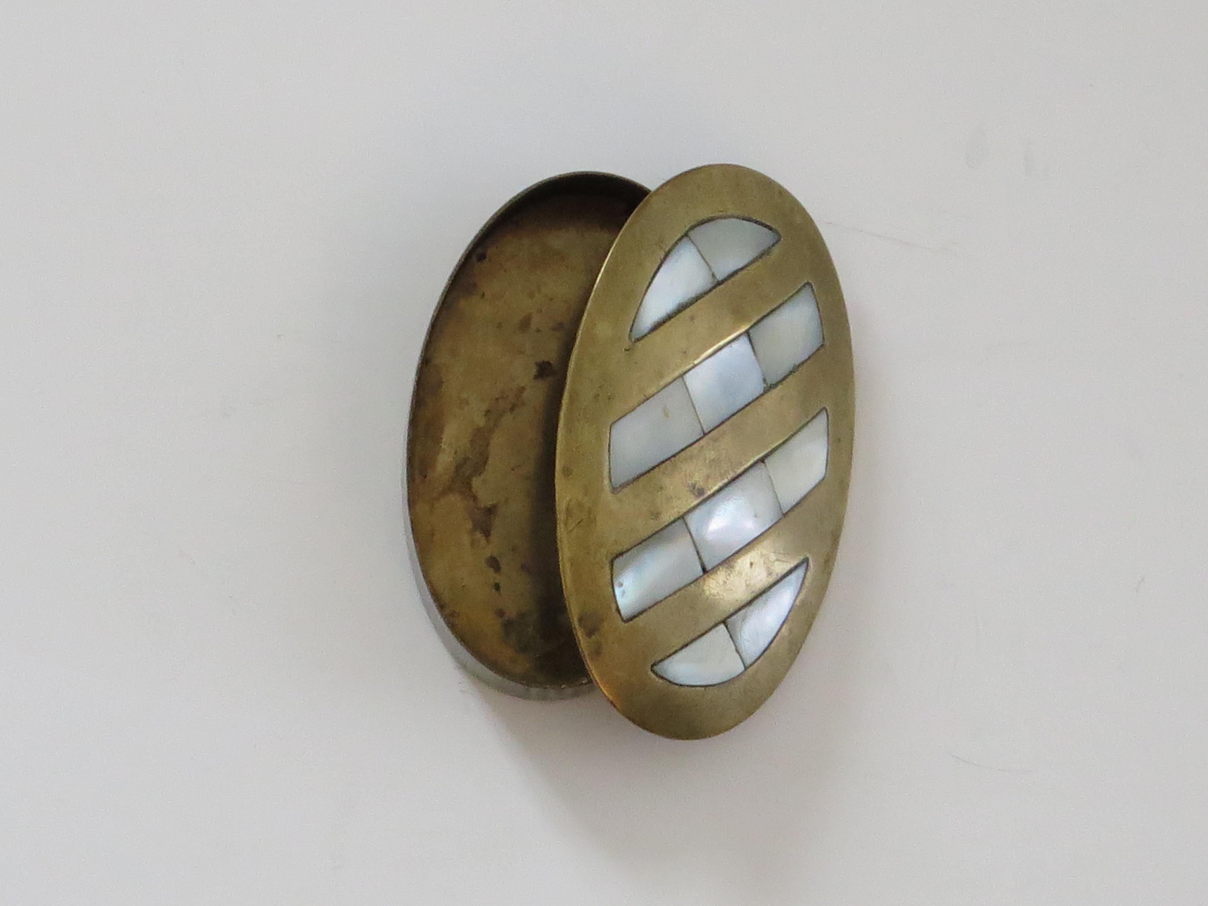 This is a small oval shaped antique metal Pill Box with Mother-of Pearl Inlay dating to the Edwardian or late Victorian period.

The box is made of bronze / brass as an oval shape with a lid that is slightly curved to the top. The lid top has