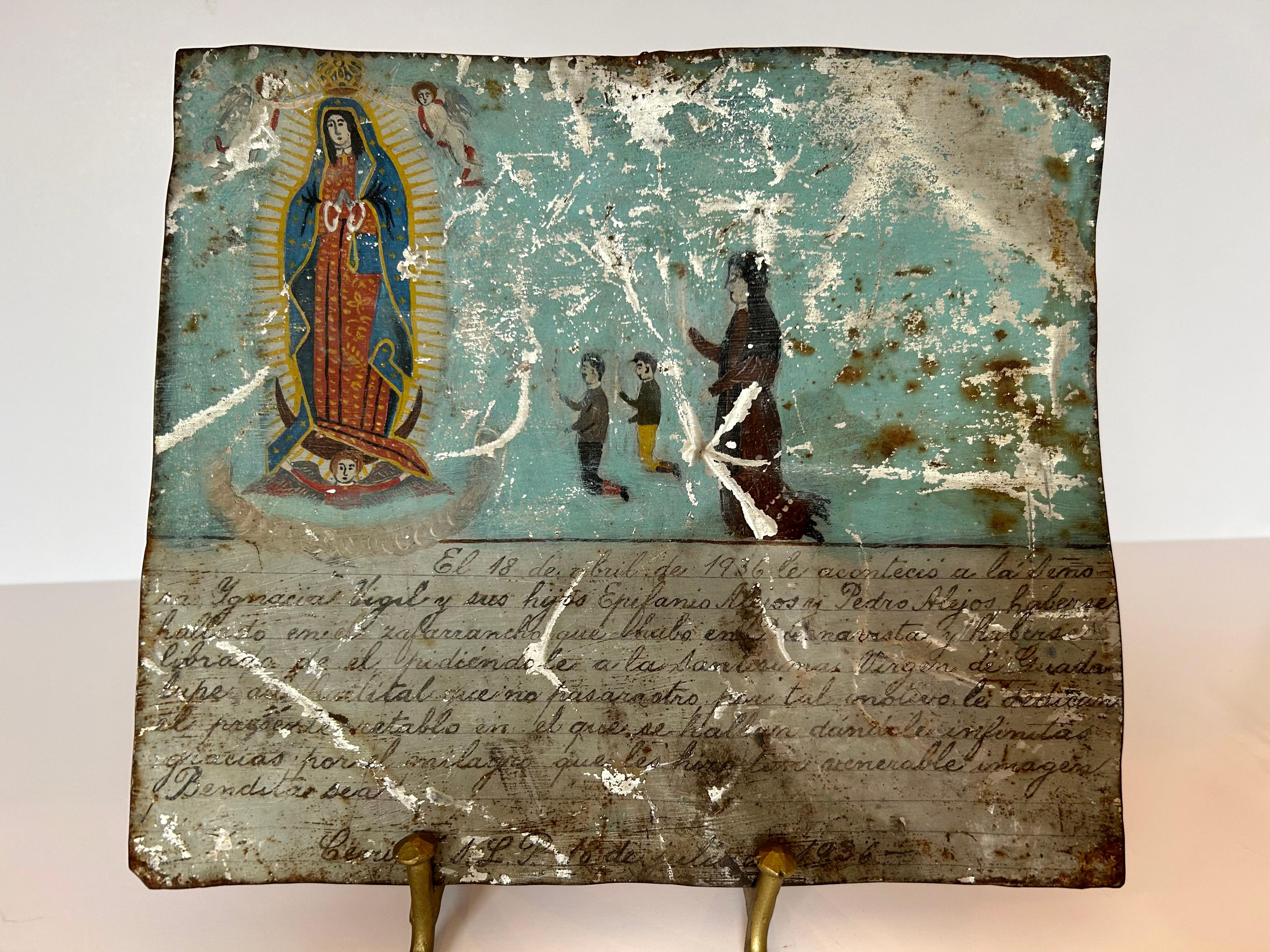 Beau retablo ou ex voto mexicain, peint en 1936, décrivant une mère remerciant la Vierge pour la sécurité de ses deux garçons. La Vierge couronnée de la Guadeloupe flotte entourée de rayons de lumière et de trois anges, tandis que la mère est