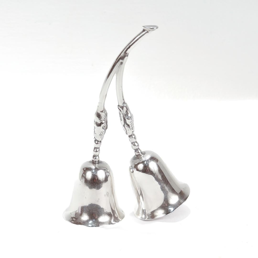 A fine Mexican sterling silver double bell.

With a curved handle that supports two small bells reminiscent of a pair of flowers or fruit on the vine. 

Designed so that it can rest on either bell.

Marked to the interior of each bell cup.

Simply a