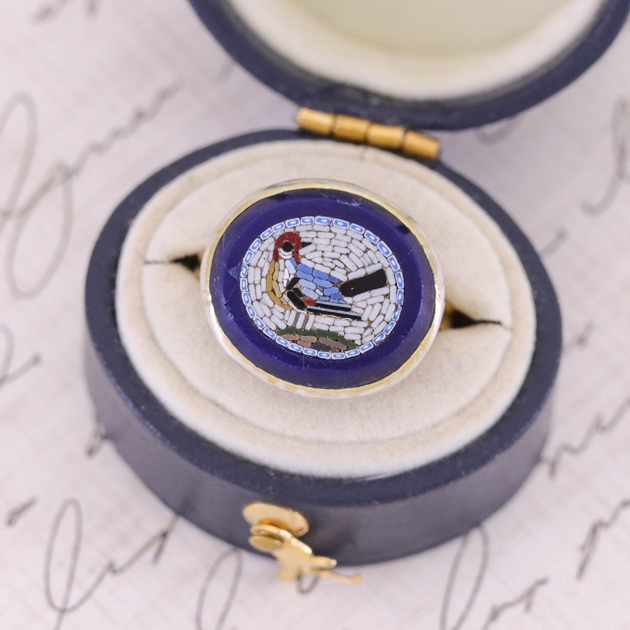 A marvelous ring featuring a micromosaic of a bird -- possibly a red headed woodpecker.

The mosaic was originally an antique silver pin (circa 1880) transformed by backing the piece in gold, and adding a 14k gold mounting.

The face of the ring