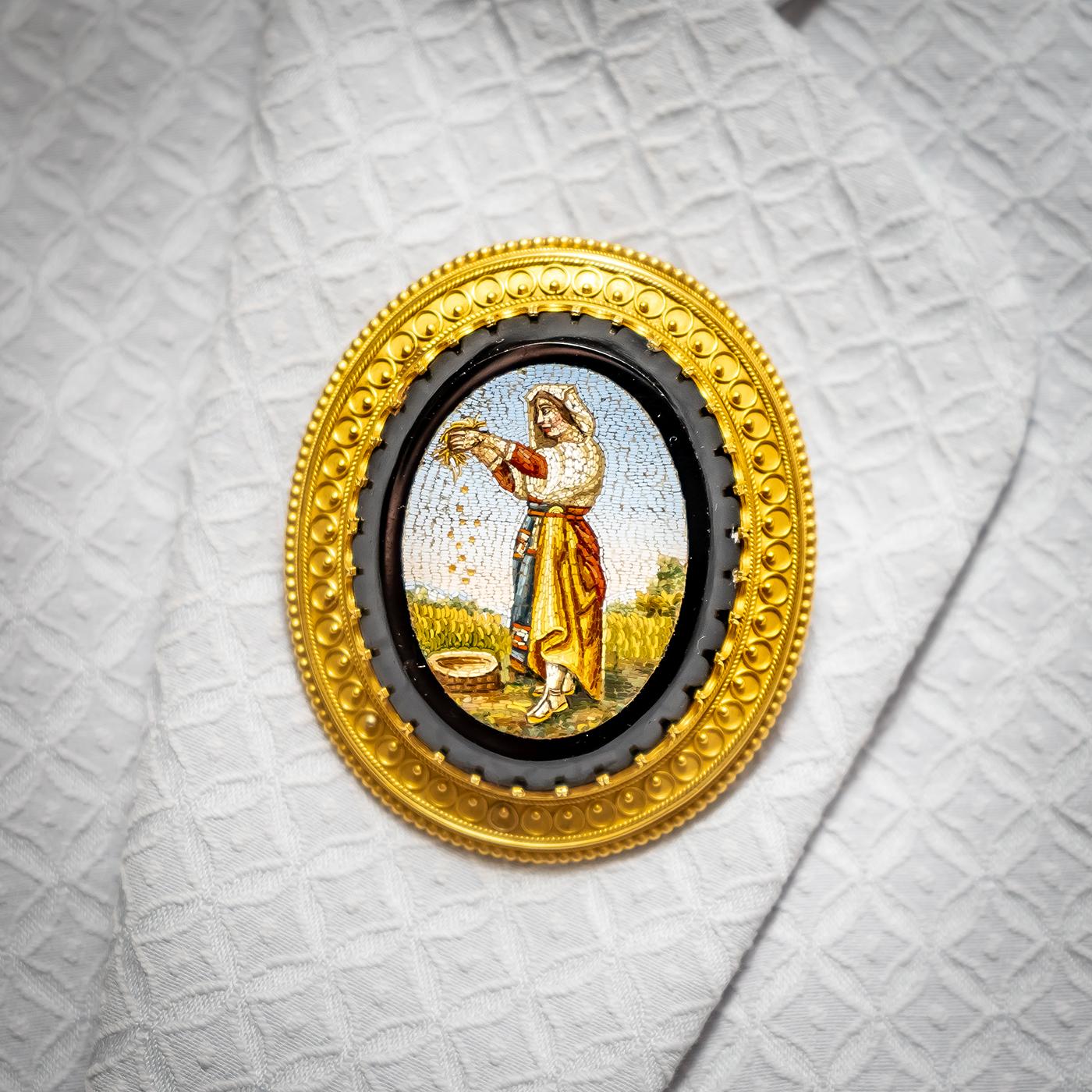 An antique micromosaic brooch, oval image depicting a woman farming crops, backed on black onyx, in an 18ct yellow gold Etruscan style border, with rope and beaded edge detail. Circa 1870's, measure approximately 49 x 58mm
Micromosaic jewellery
