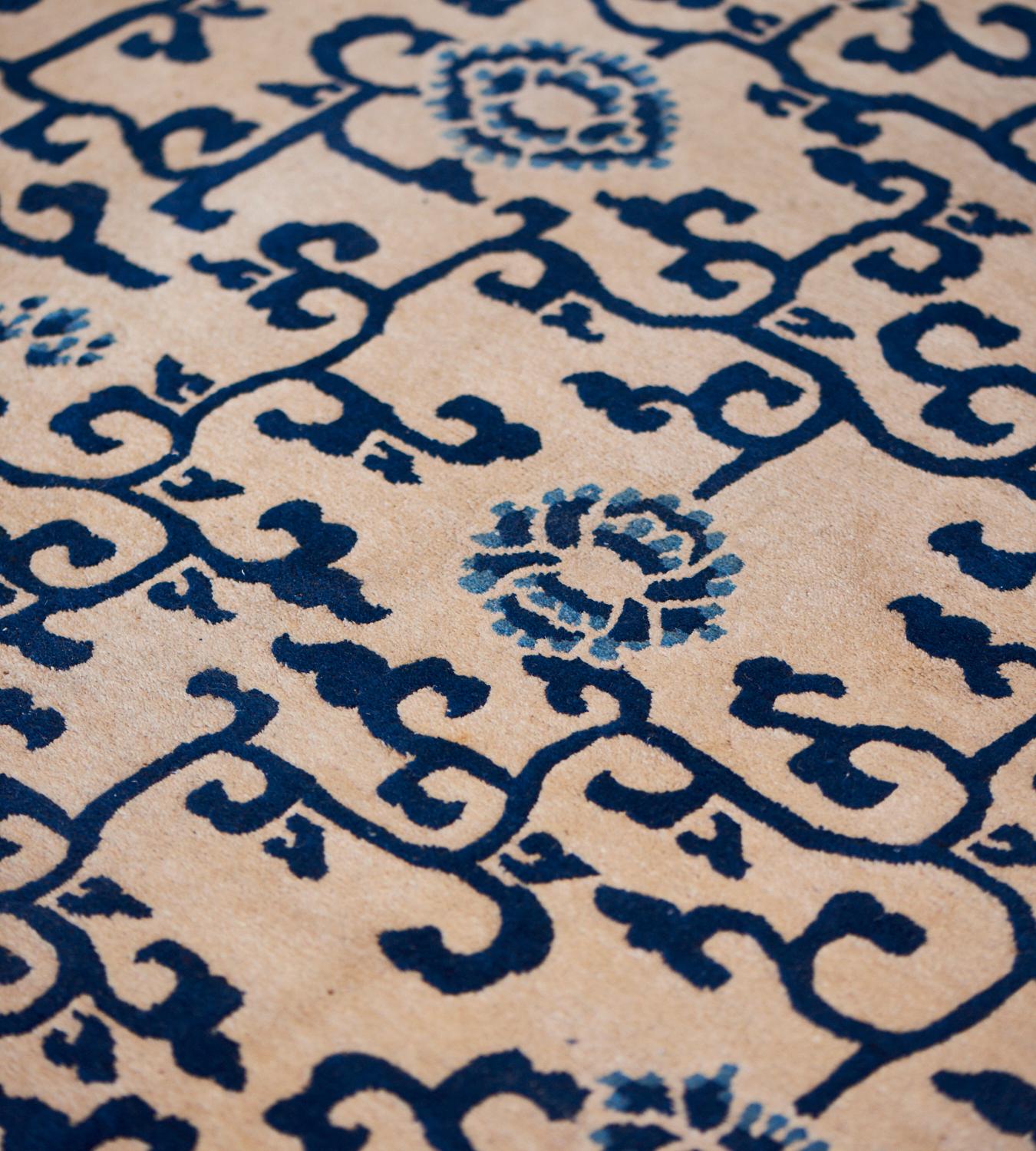 This antique, circa 1900, Chinese Peking rug has an ivory field with an overall design of indigo-blue angular scrolling vine issuing light blue and indigo-blue flowerheads, in an ivory and indigo-blue interlocking lattice-weave border, inner ivory