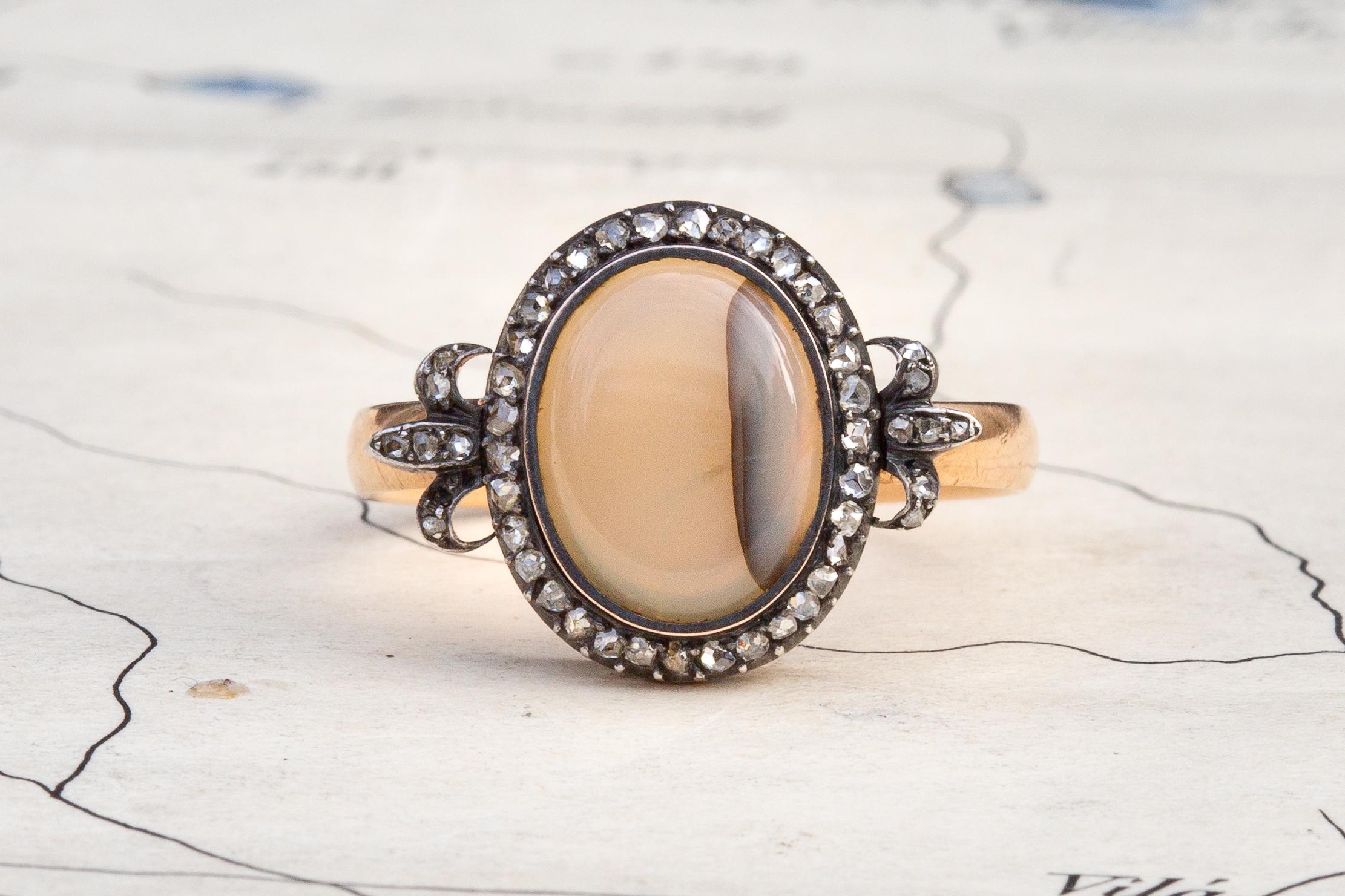 This stunning antique cluster ring was made in France and dates to around the mid 19th century, circa 1860. In the centre rests a smooth banded agate in an open back setting, encircled by a halo of rose cut diamonds in closed-back, cutdown silver