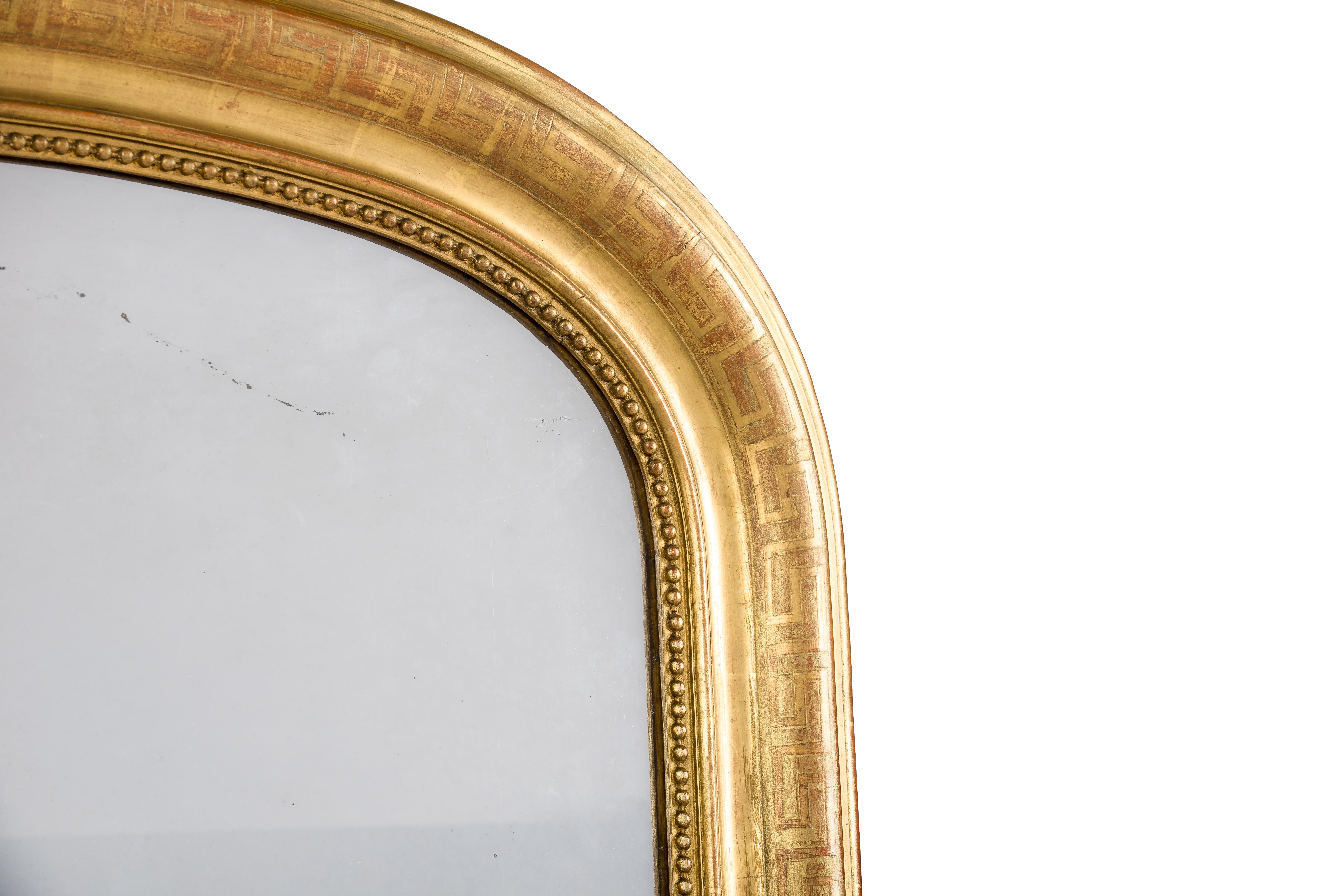 This beautiful antique mirror with an arched top was made in France circa 1850. It has upper rounded corners typical for the Louis Philippe style. The mirror has a solid pine base smoothened with gesso. An engraved Greek key pattern enriches the