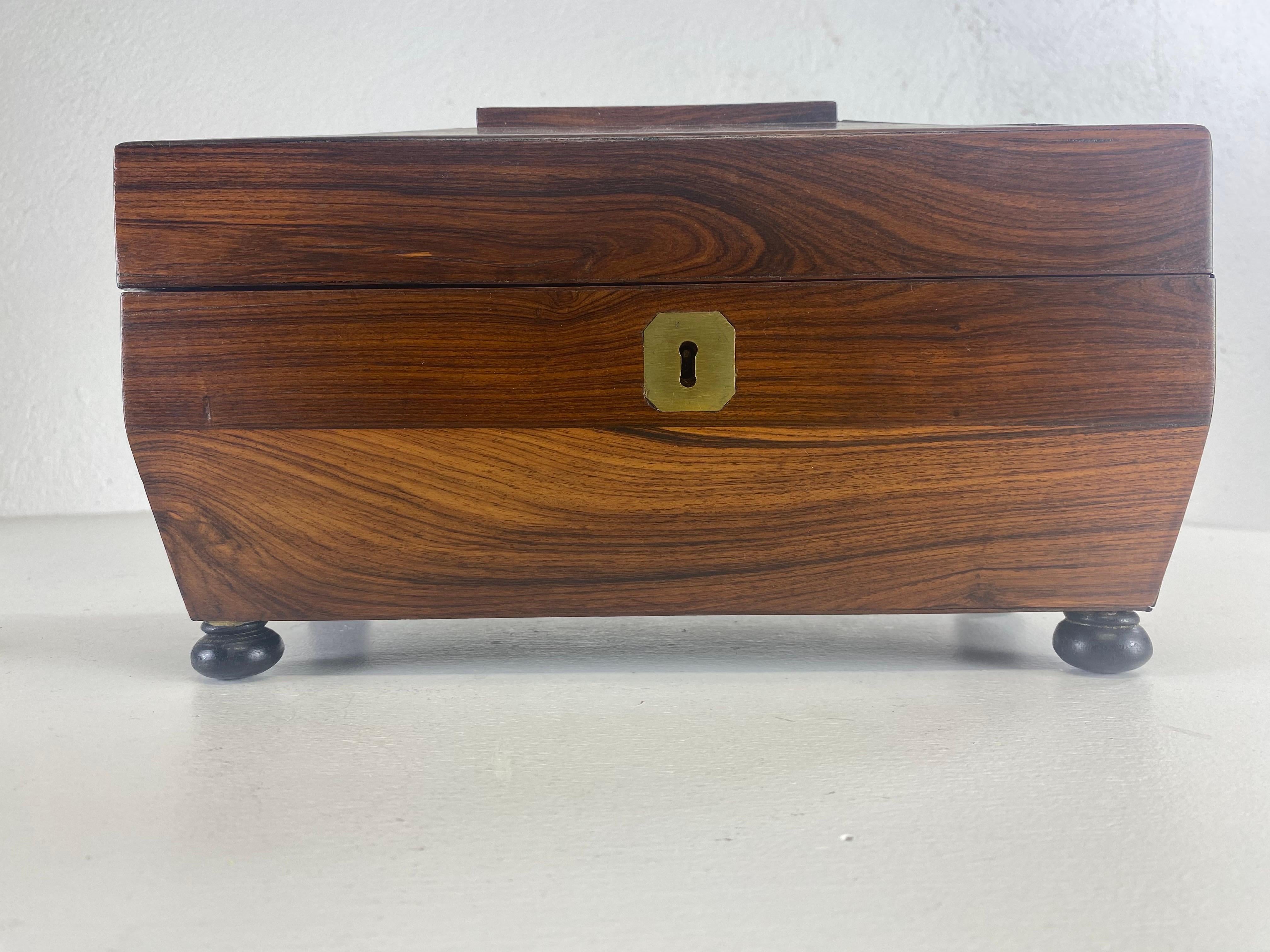 Il s'agit d'une boîte à thé en bois de rose fabriquée à la main au 19e siècle. Cette boîte à thé est dotée d'un verre jetable au centre et de deux compartiments de part et d'autre. La boîte à thé repose sur quatre pieds noirs en forme de chignon et