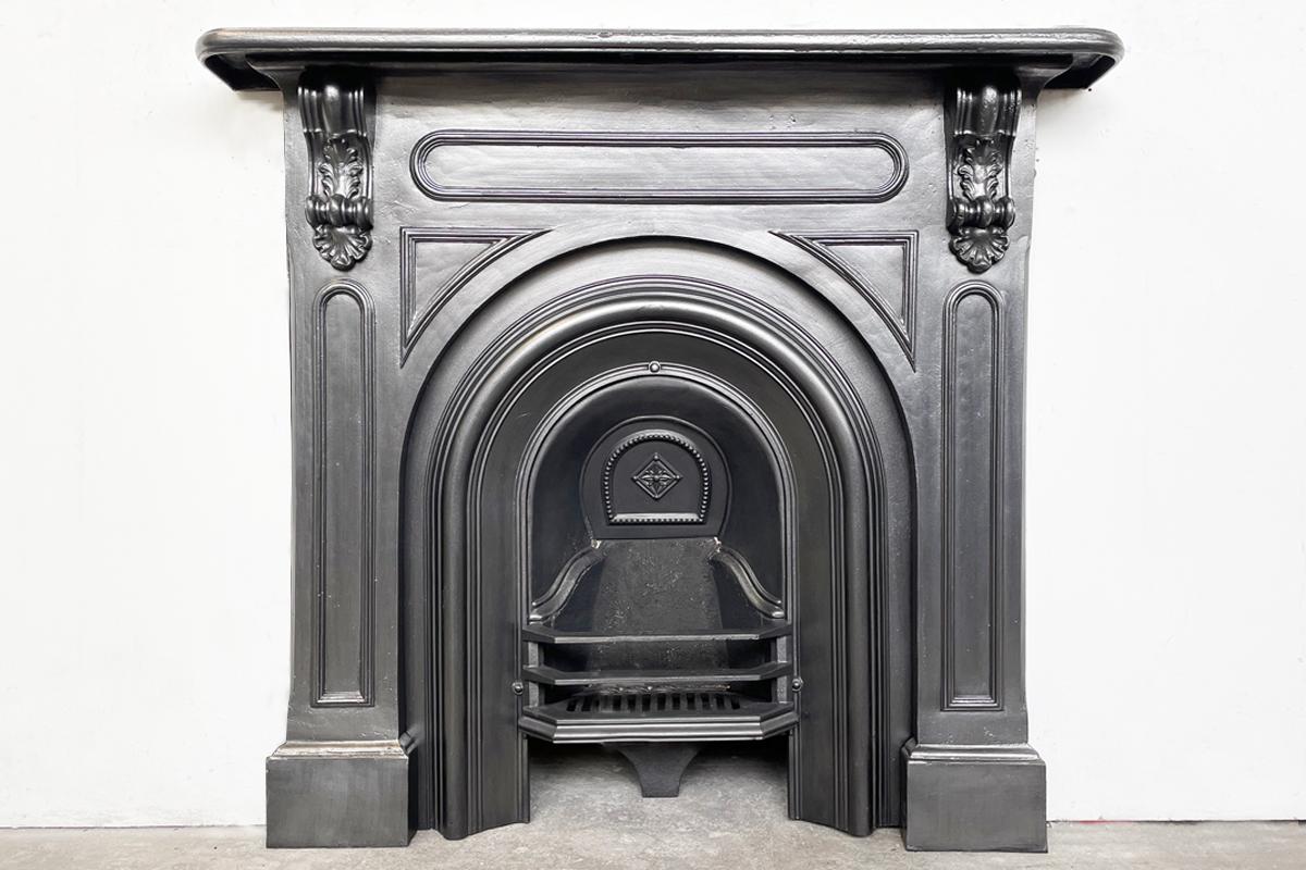 Antique mid 19th century Victorian cast iron fireplace surround with arched aperture and cast corbels supporting the shelf. Circa 1870.

Finished in traditional black grate polish. Pictured with an original arched fireplace grate, priced