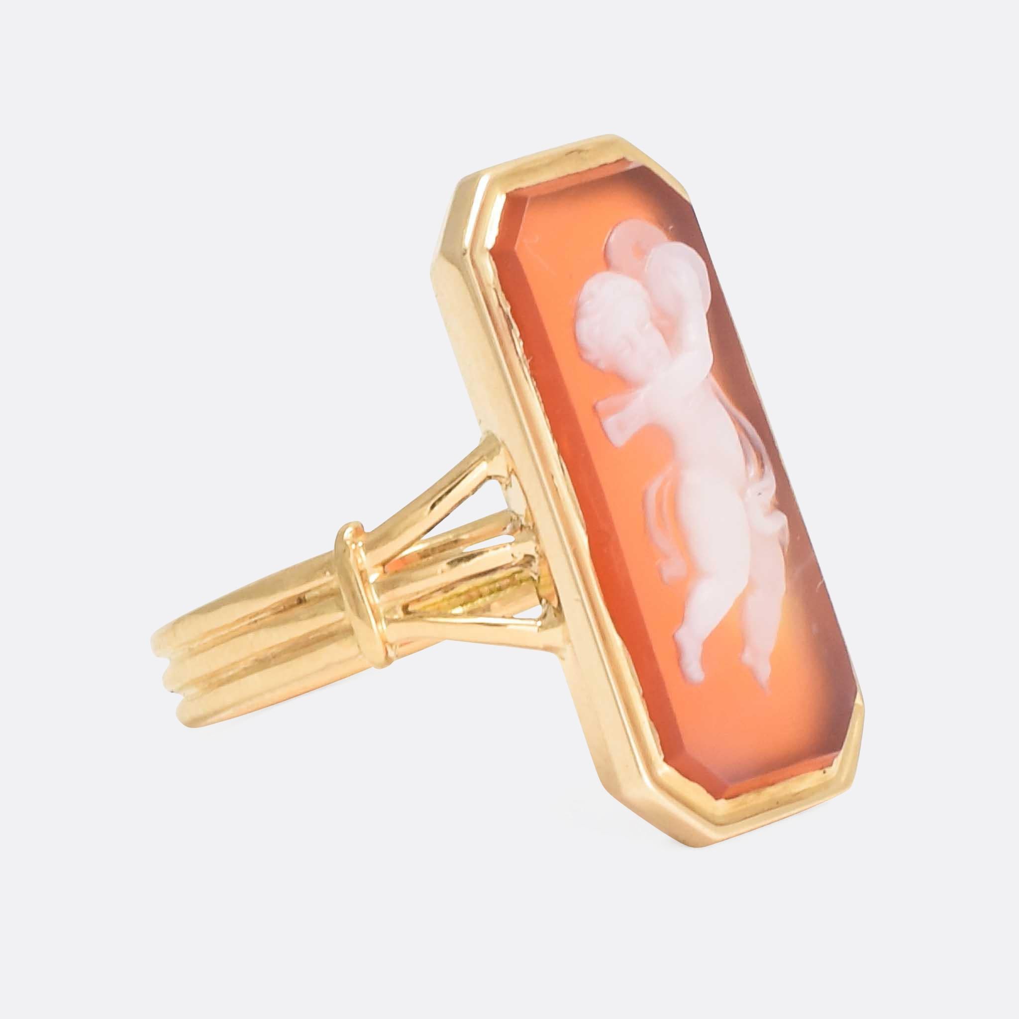 A cool antique cameo ring, the red and white sardonyx stone has been expertly carved to depict Cupid with Cymbals. The ring itself is modelled in 18k gold, with a reeded band and trifurcated shoulders - it dates from the mid 19th Century, circa