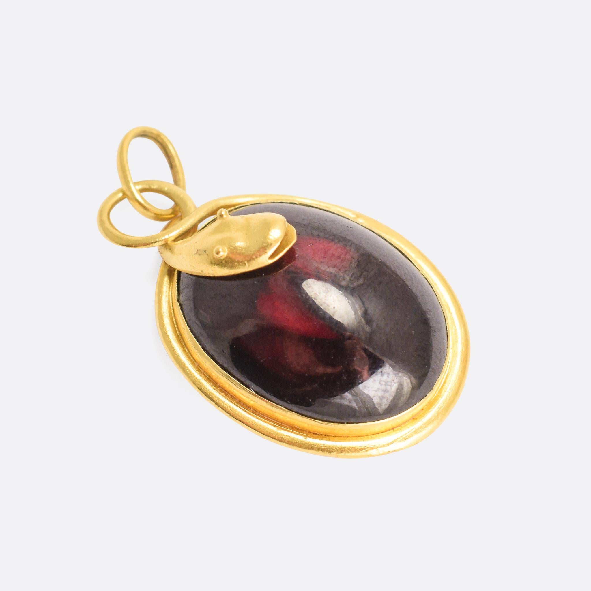A gorgeous mid-Victorian pendant modelled as a cartoonish snake coiled around a large oval garnet cabochon prize. The stone is foil-backed, meaning that the light reflects back through it showing off the deep red colour. Modelled in 15k yellow gold,